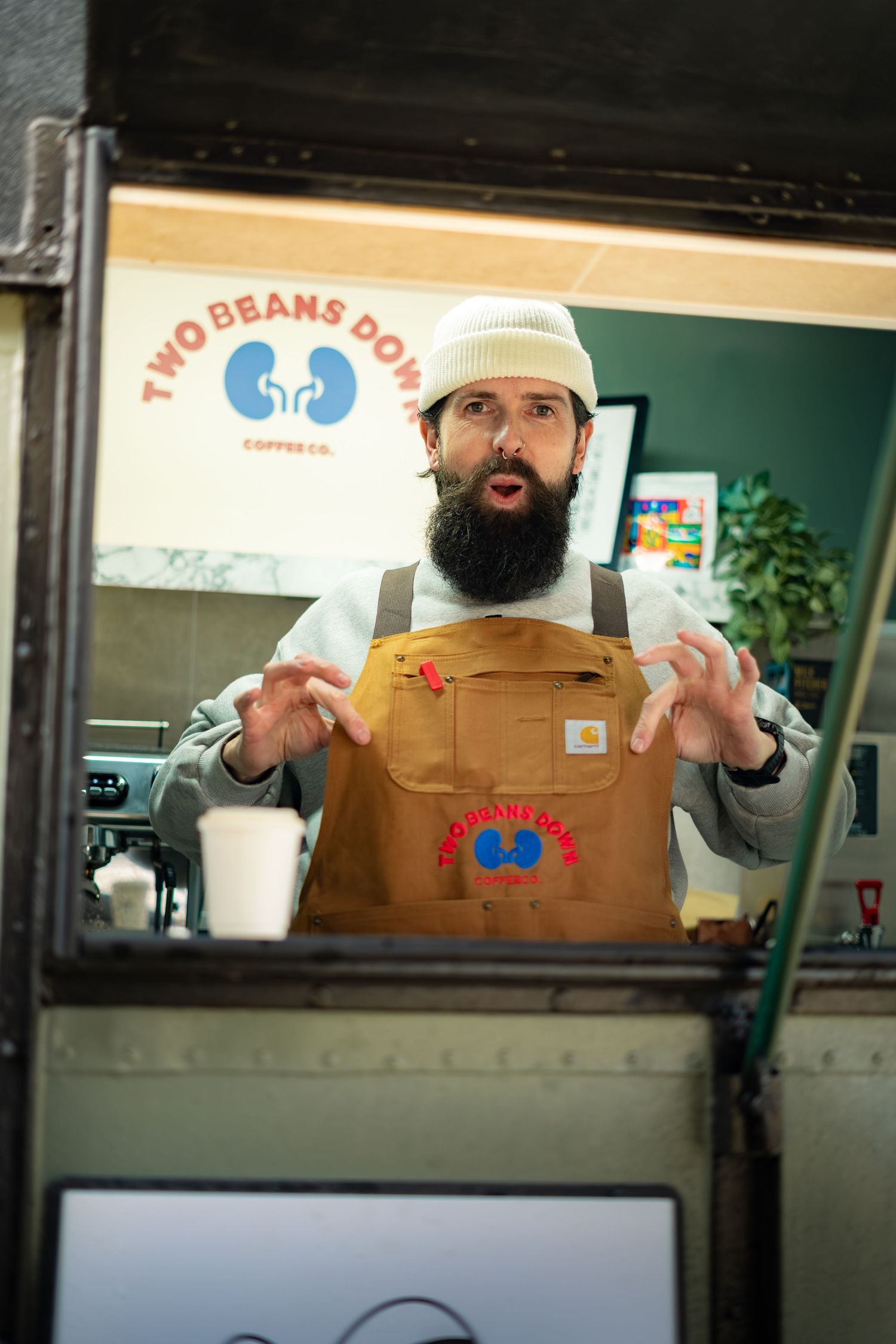 Expressive bearded barista gesturing inside Two Beans Down Coffee Co. mobile coffee truck.