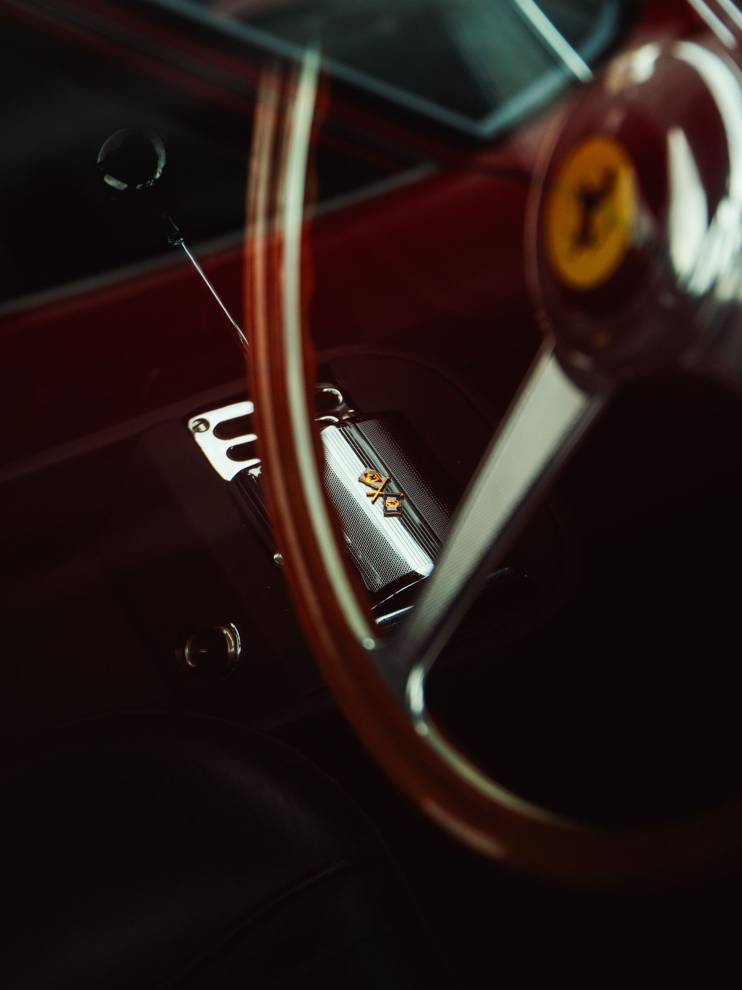 Vintage Ferrari classic car interior featuring wooden steering wheel with prancing horse logo badge.
