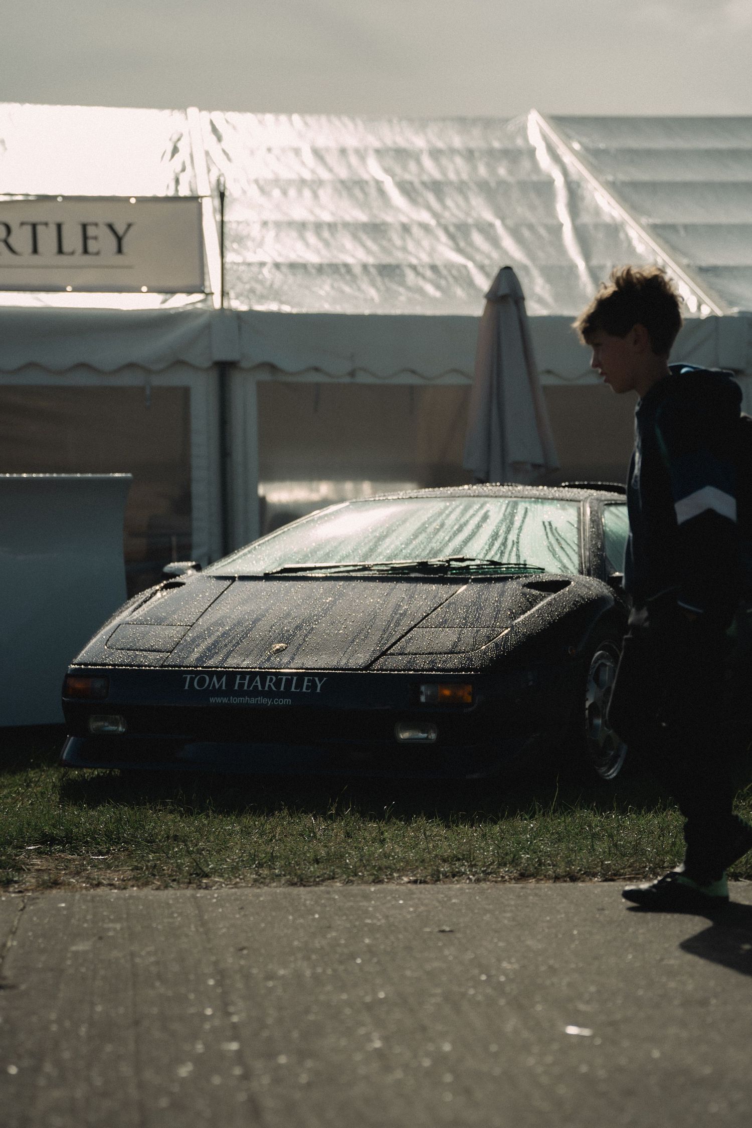 A muddy black Lamborghini Diablo with Tom Hartley branding parked on grass near white event tents.