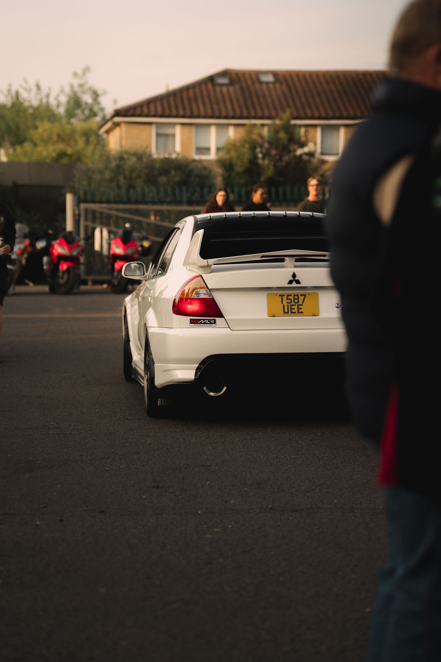 White Mitsubishi Lancer Evolution with UK license plate T587 UEE parked at a car meet during golden hour.