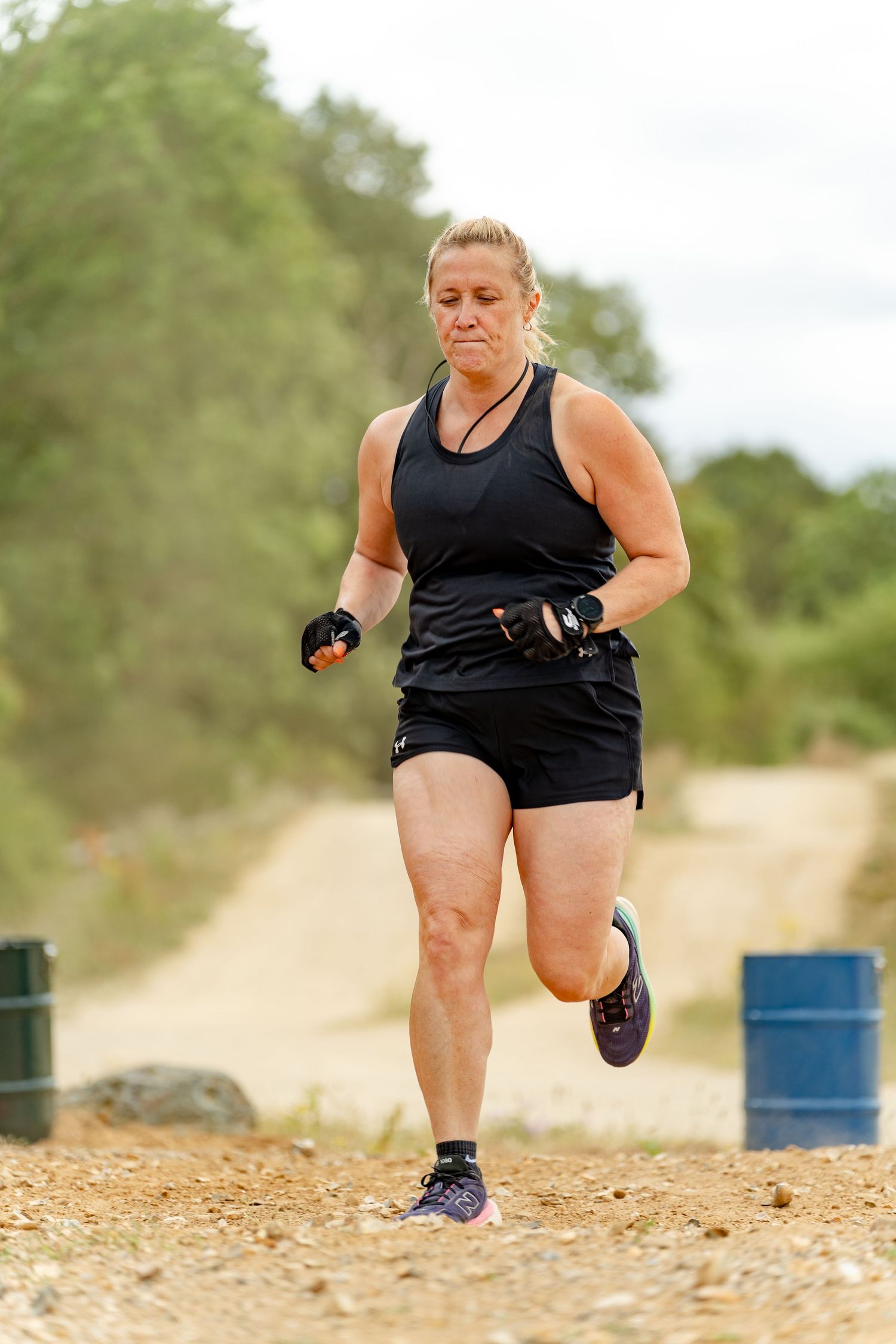 Woman in black athletic wear running on a dirt trail during an outdoor race or obstacle course event.