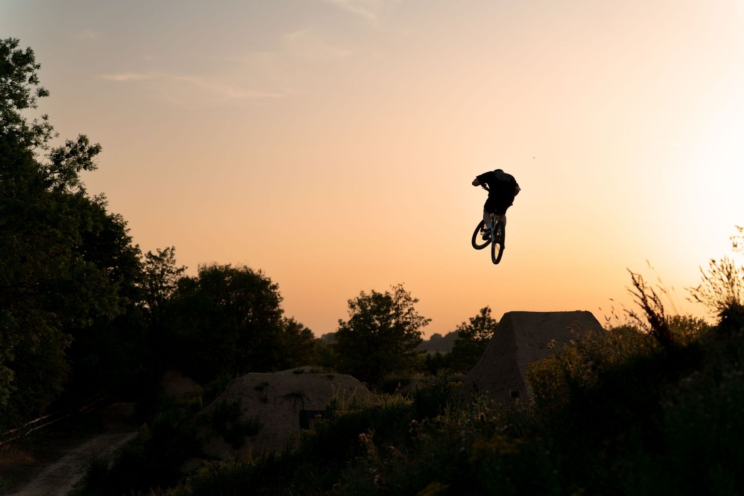 Silhouette of a BMX rider performing a jump trick against a vibrant orange sunset sky.
