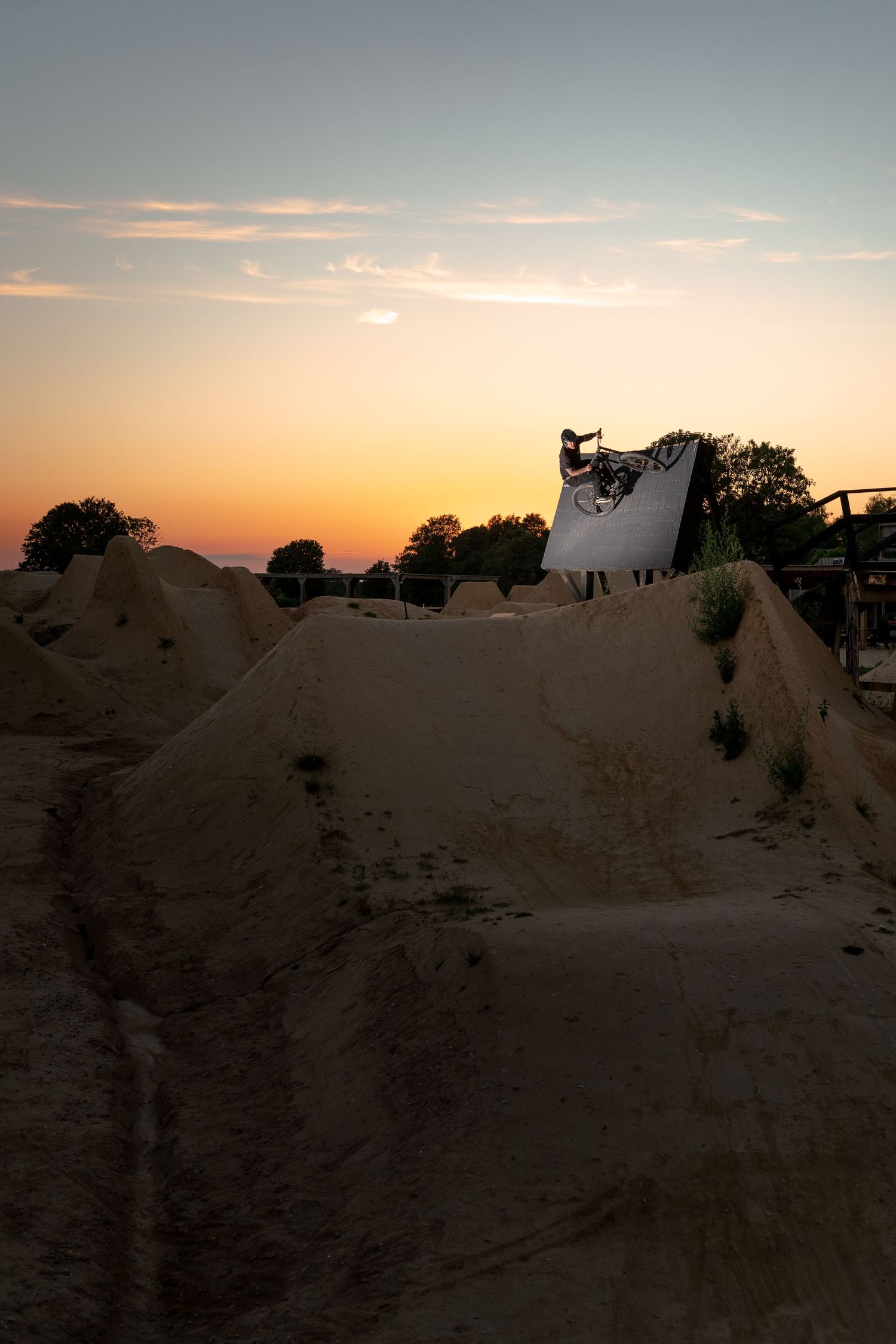 Silhouette of a BMX rider on a ramp at a dirt bike park during a colorful dusk sunset.