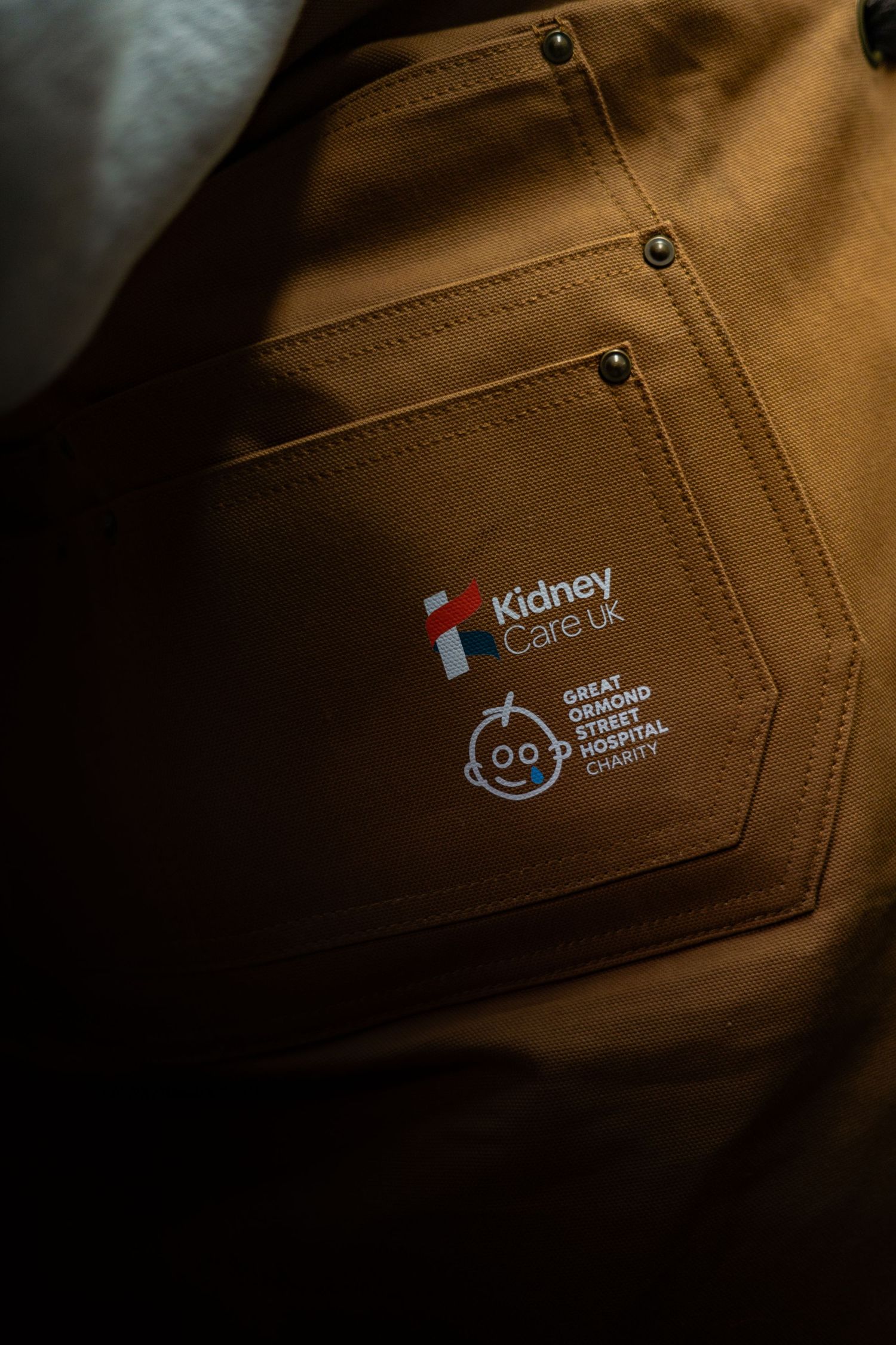 Close-up of Carhartt apron pocket featuring Kidney Care UK and Great Ormond Street Hospital logos.