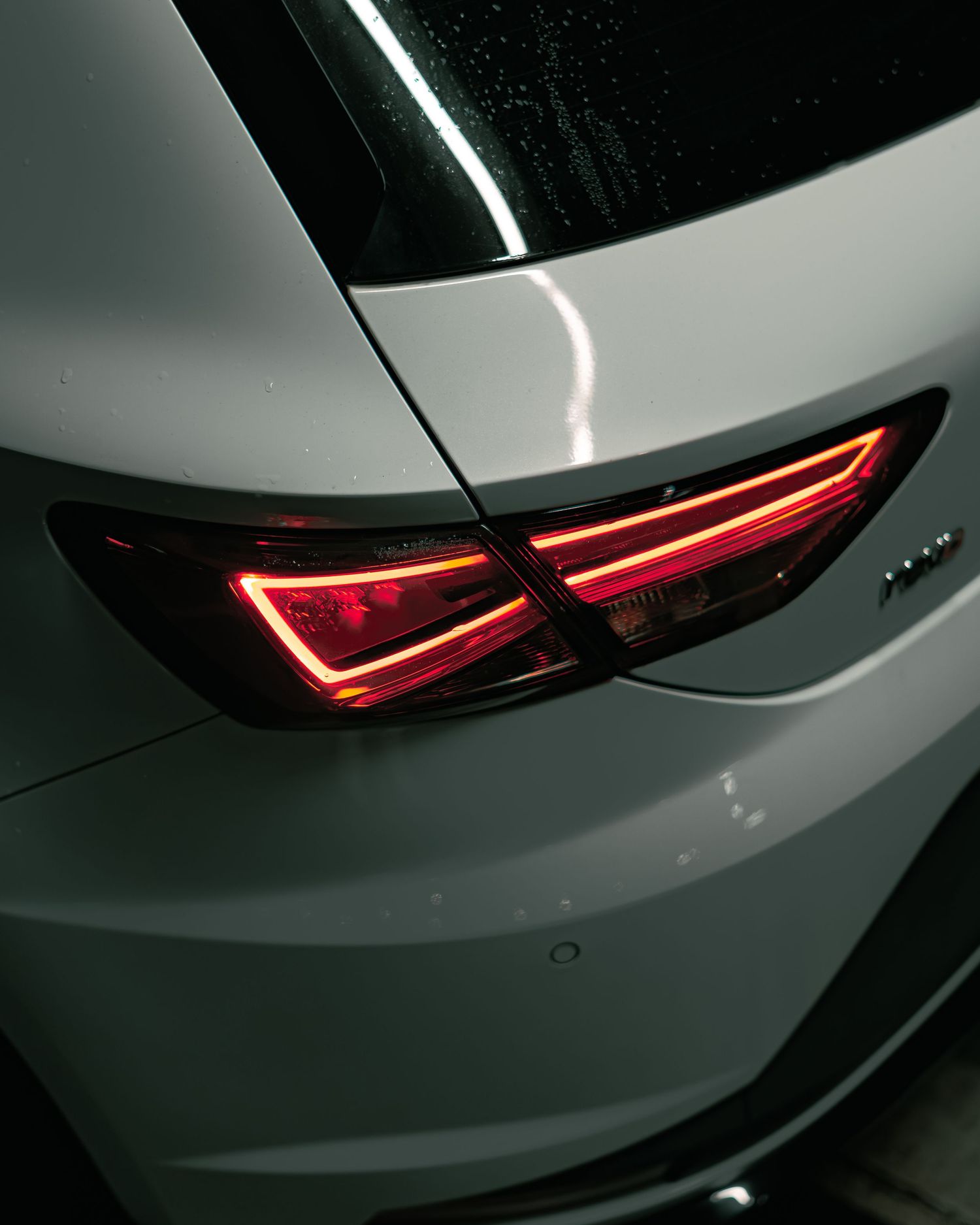 Close-up of red LED tail lights on a white SEAT Leon Cupra in a dark environment.