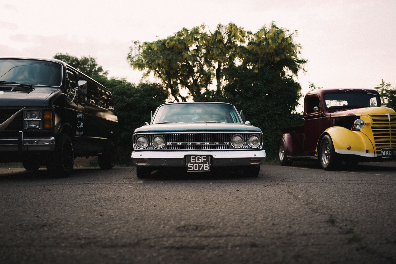 Three classic vintage cars parked side by side at a car show, including a white 1960s Chevrolet truck with license plate EGR 9078.