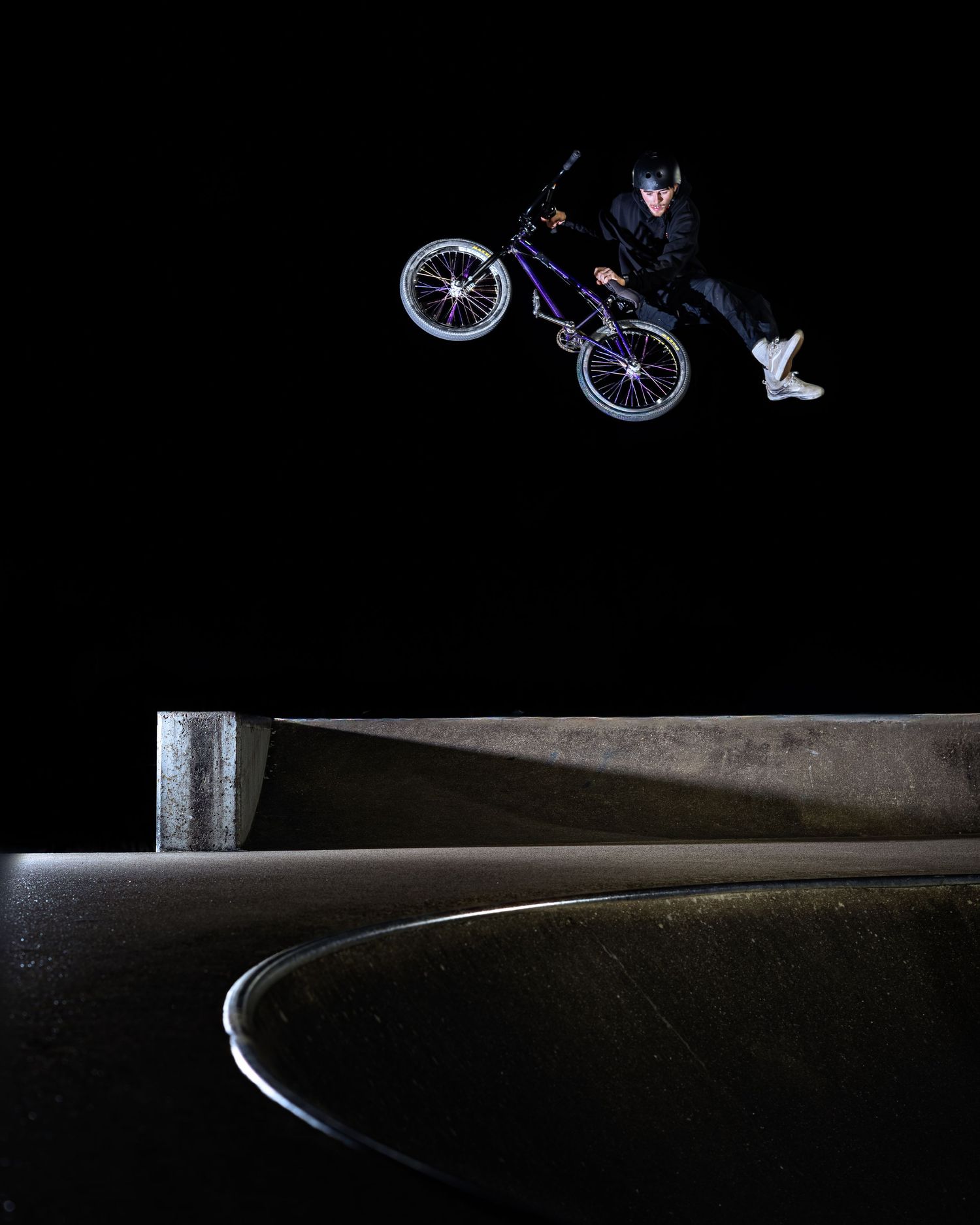 BMX cyclist executing an impressive night jump over a concrete skatepark ledge.