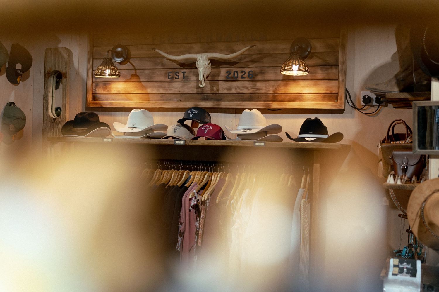 Rustic western boutique displaying cowboy hats on wooden shelves beneath a longhorn skull sign with warm lighting.