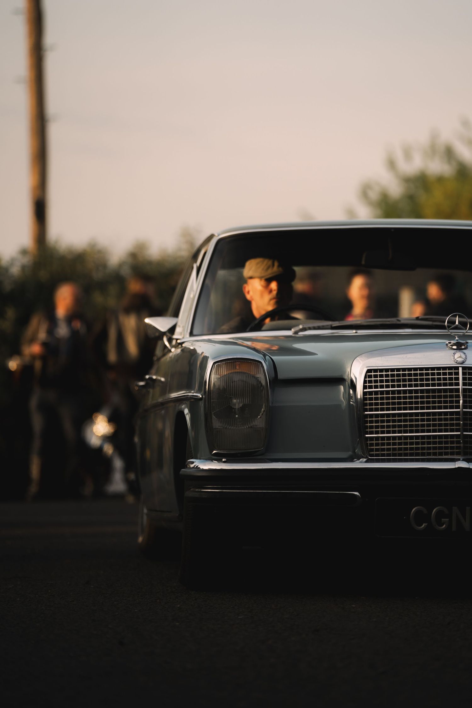 Vintage Mercedes-Benz classic car front view with chrome grille, parked at dusk with people gathered in background.