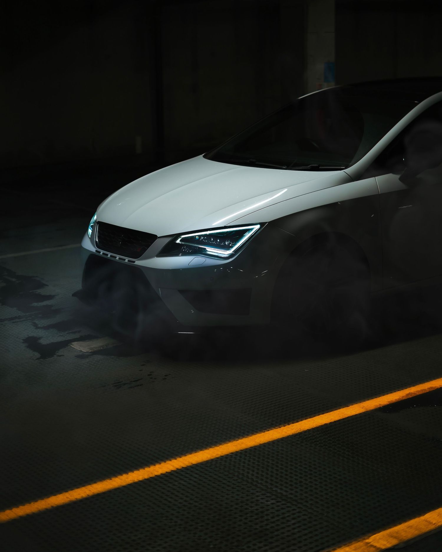 White SEAT Leon Cupra photographed in a dark parking garage with dramatic lighting and smoke effects.