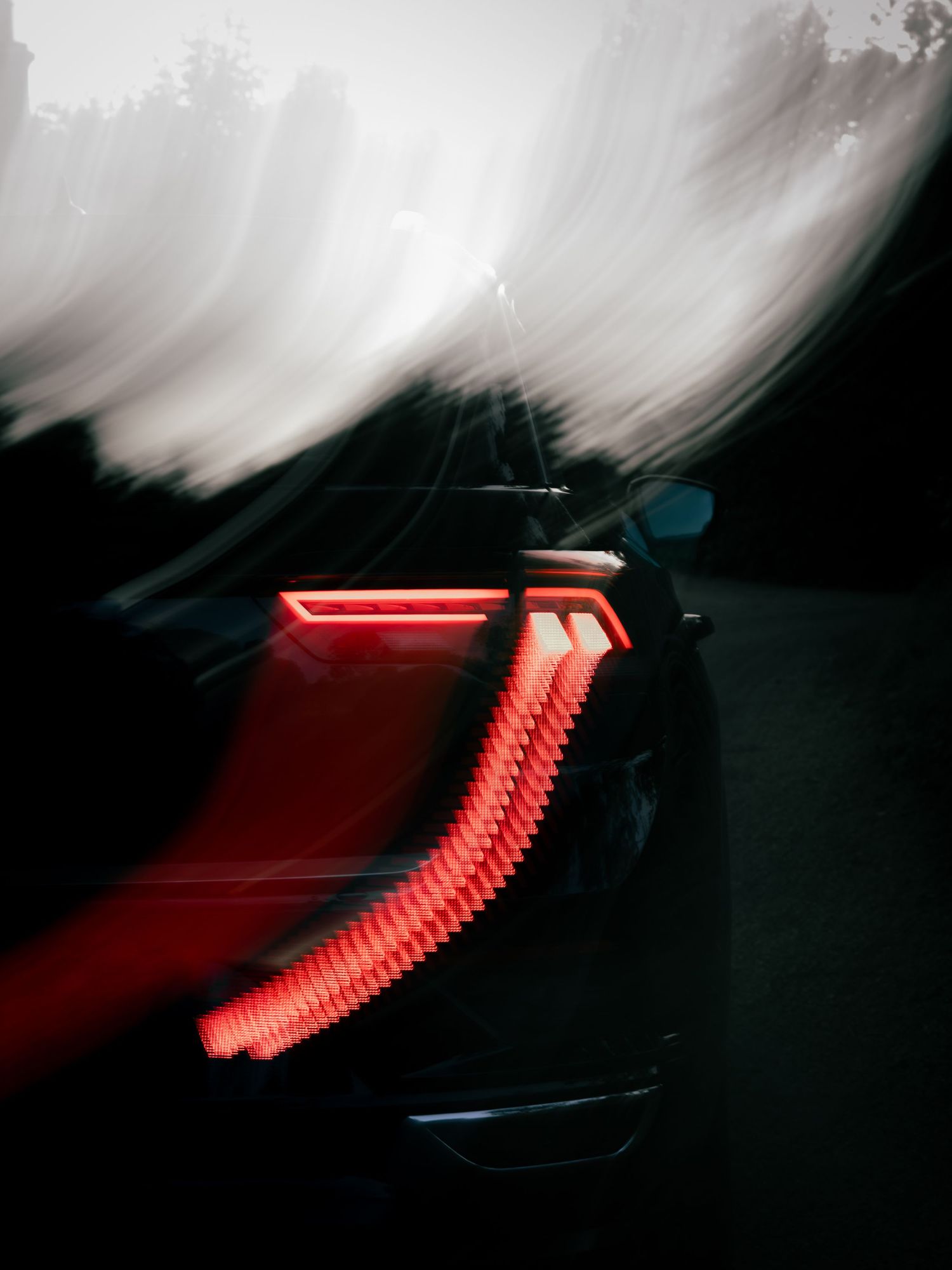 Blurred motion shot of a car's red LED tail lights streaking through darkness at night.