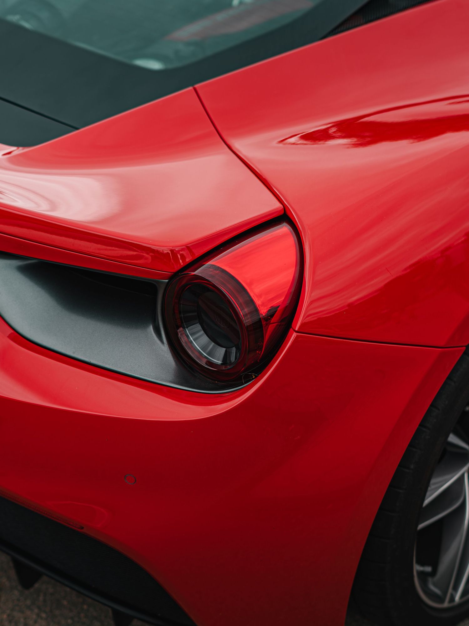 Close-up of a glossy red Ferrari's sleek tail light and curved bodywork detail.