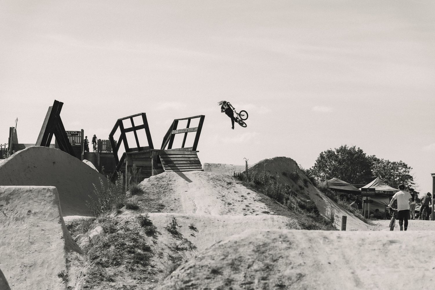 Black and white photo of BMX rider performing a high jump trick at a sandy outdoor bike park.