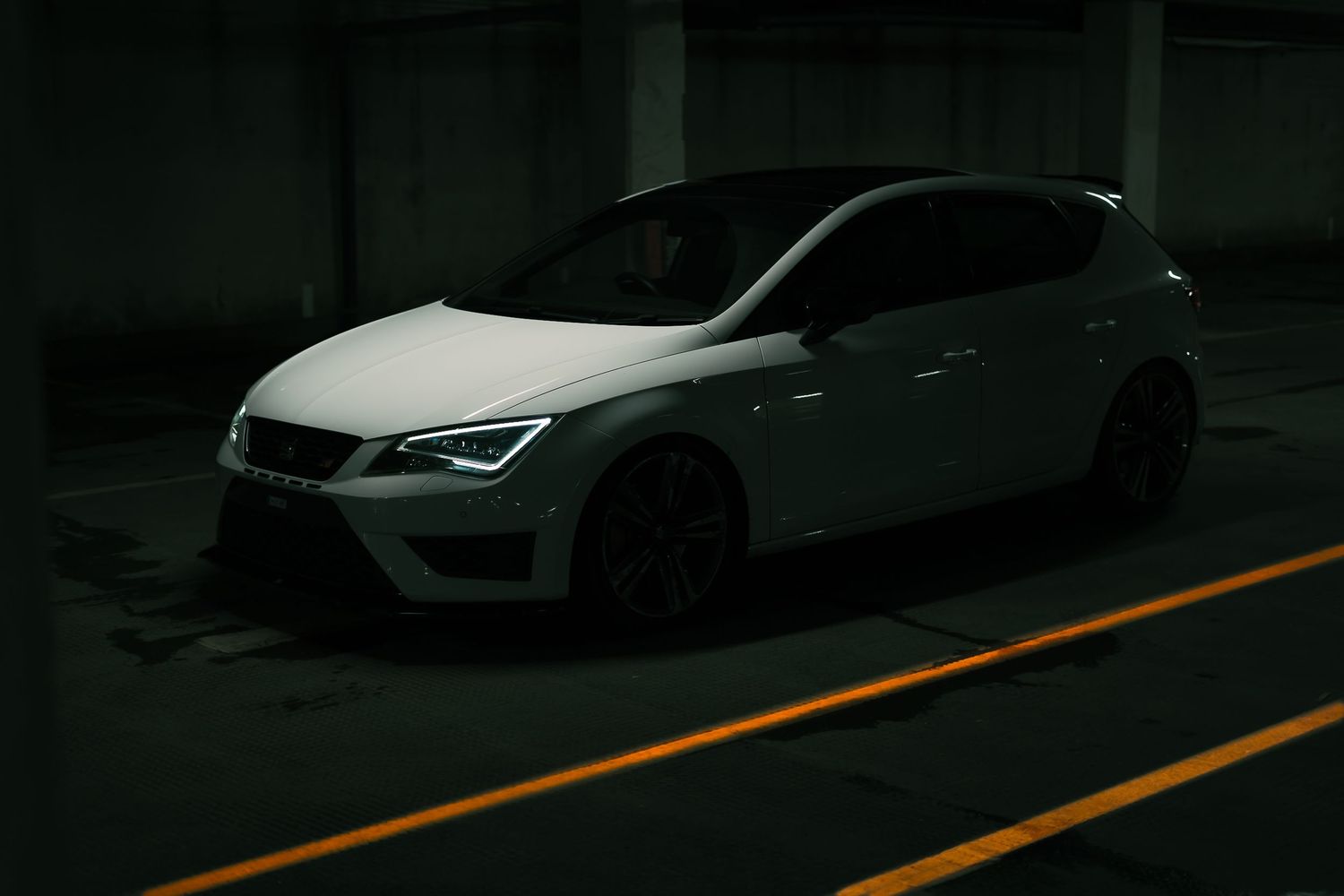 White hatchback sports car parked in a dimly lit underground parking garage.