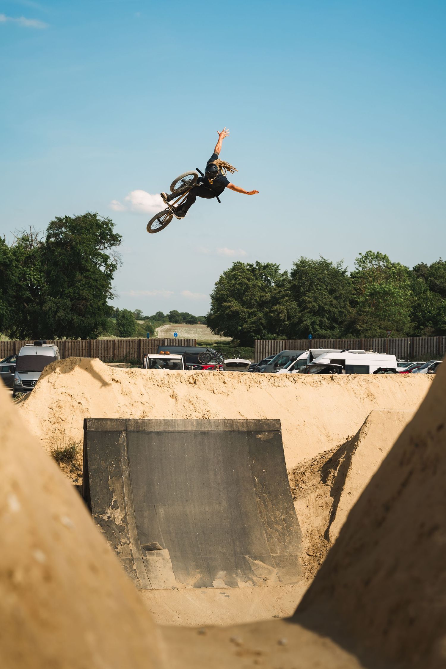 BMX rider performs a high-flying trick off a dirt ramp at an outdoor bike park on a sunny day.
