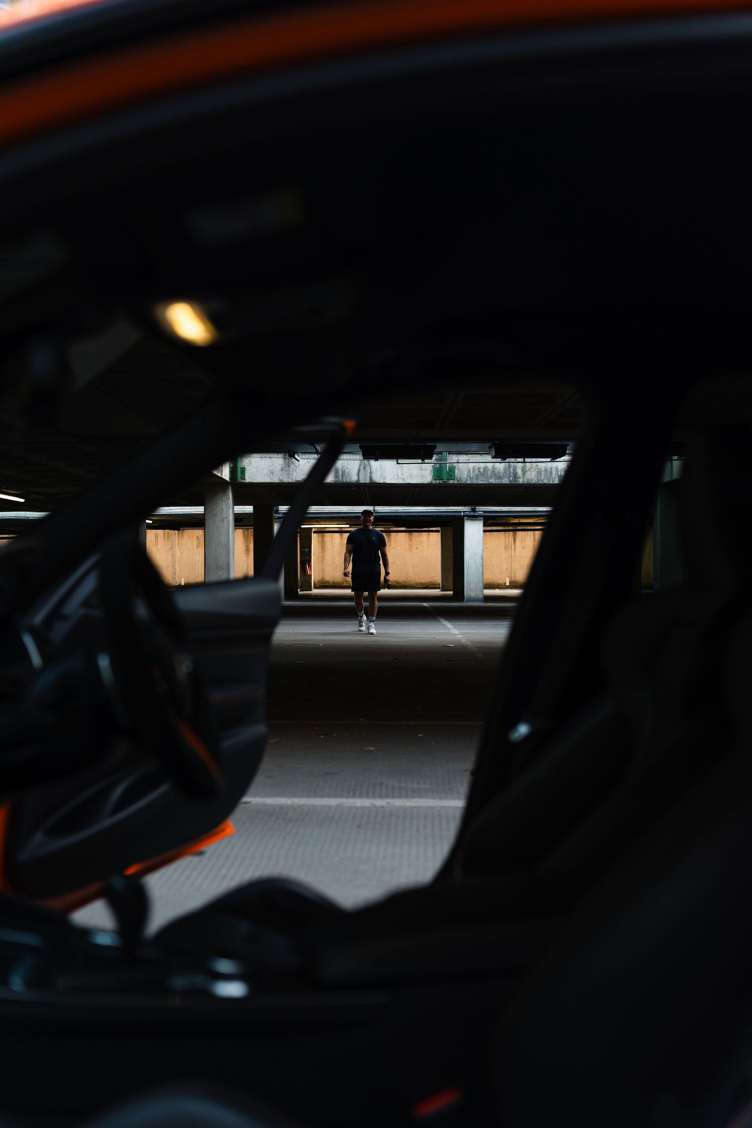 View through open car door in parking garage with person silhouetted in background near exit.