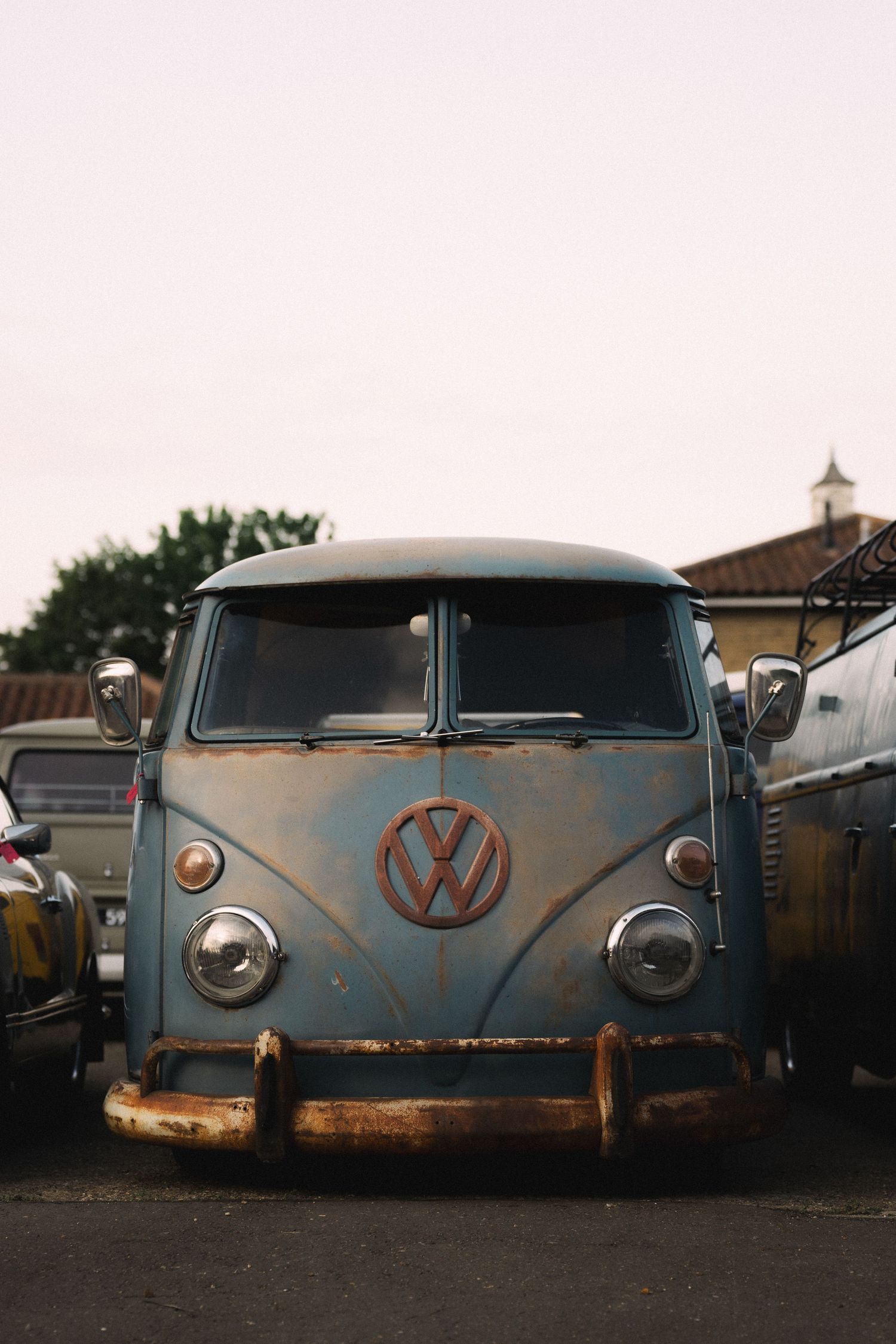 Vintage rusty Volkswagen VW Bus van parked in a lot, front view showing iconic VW logo and classic split windshield design.