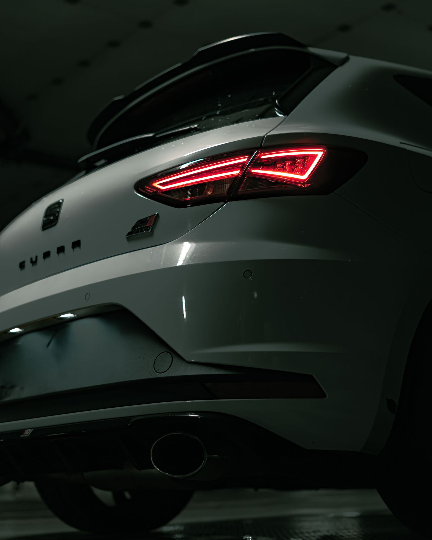 Low angle rear shot of SEAT Leon Cupra showing tail lights and exhaust in dark parking garage.