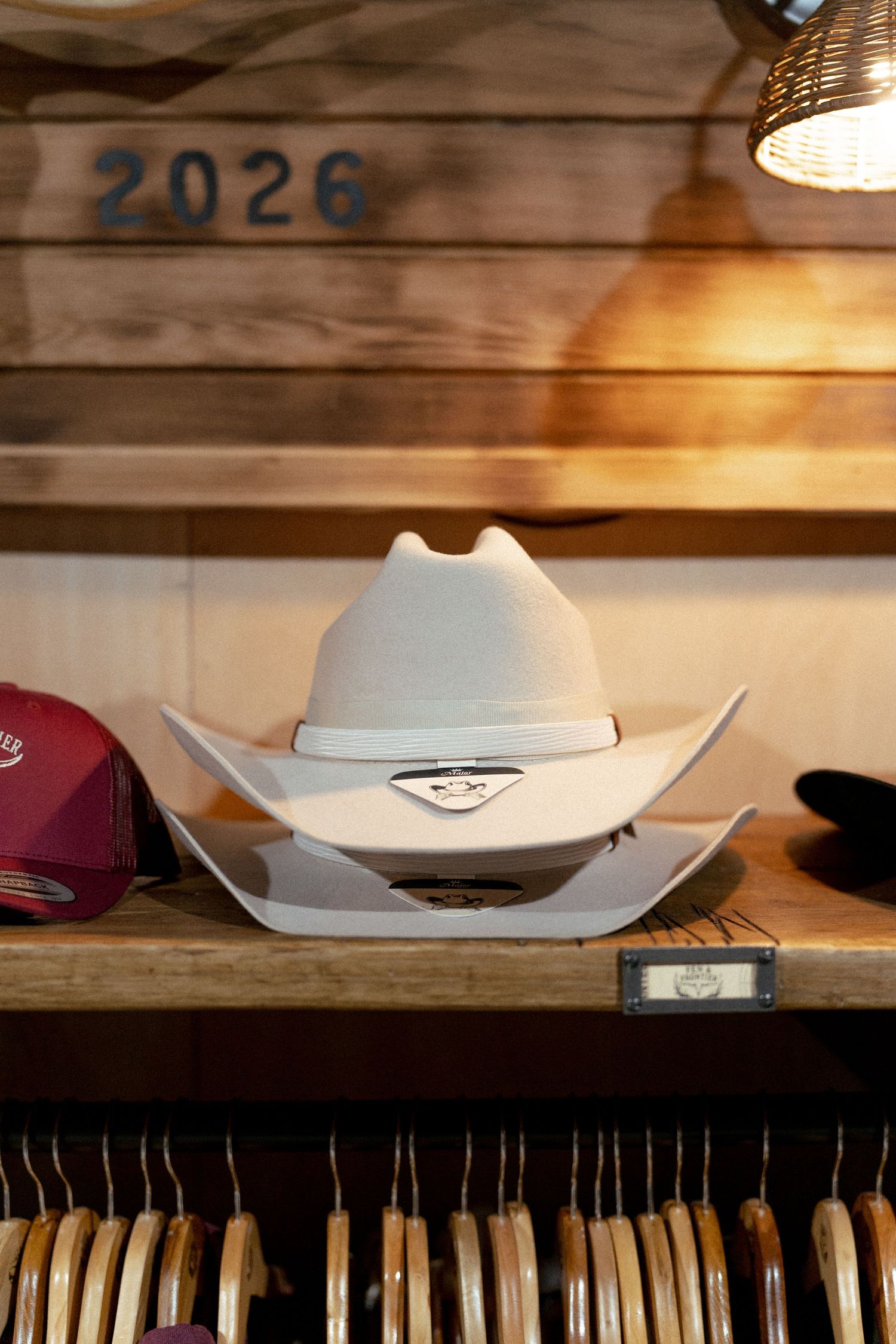 White cowboy hat displayed on wooden shelf in rustic hat shop with number 2026 on wall.