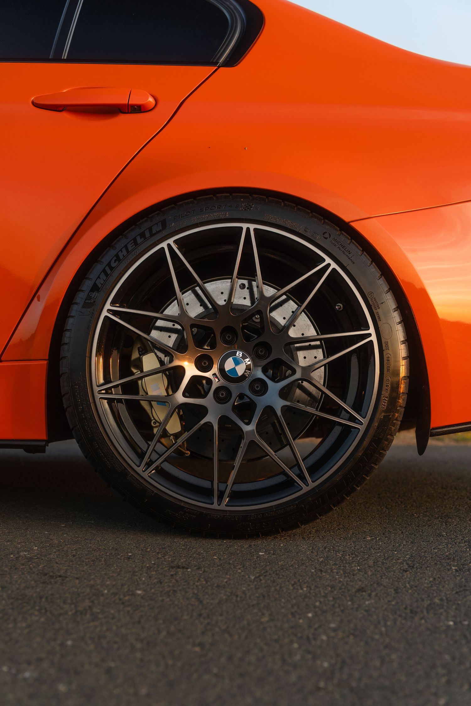 Close-up of a BMW sport car's dark alloy wheel with large brake calipers on a vibrant orange BMW coupe.