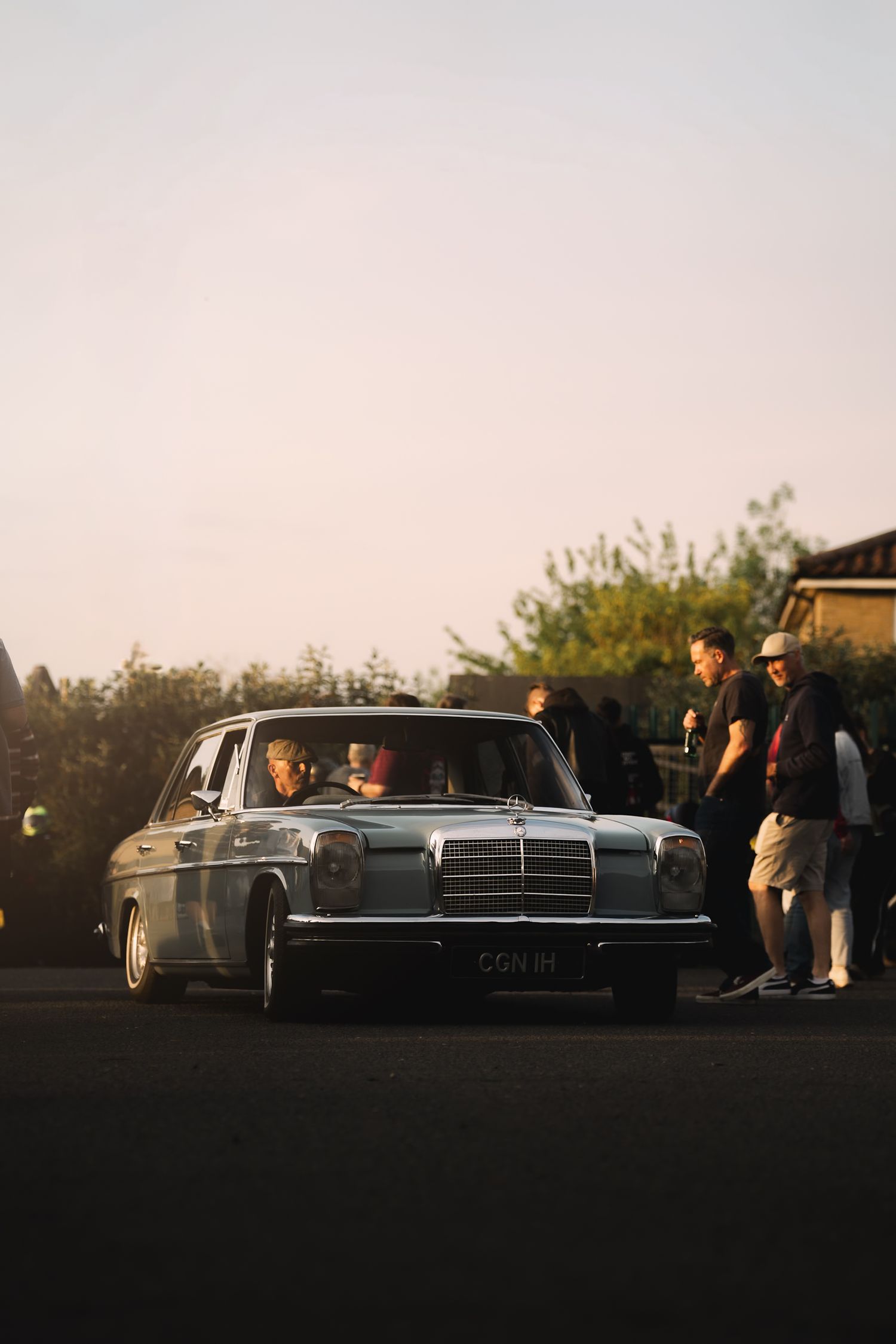 Vintage Mercedes-Benz sedan parked at golden hour with a group of people gathered around it outdoors.