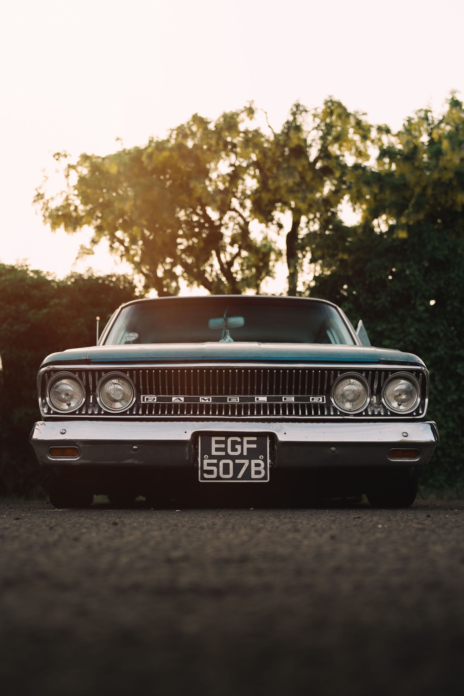 Vintage classic American car with license plate EGF 507B parked outdoors at golden hour with trees in background.