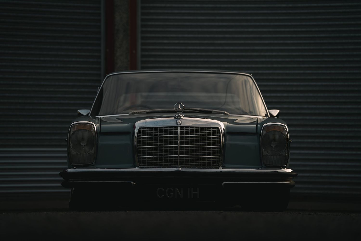 Vintage Mercedes-Benz classic car front view in dark moody lighting, parked against industrial garage doors.