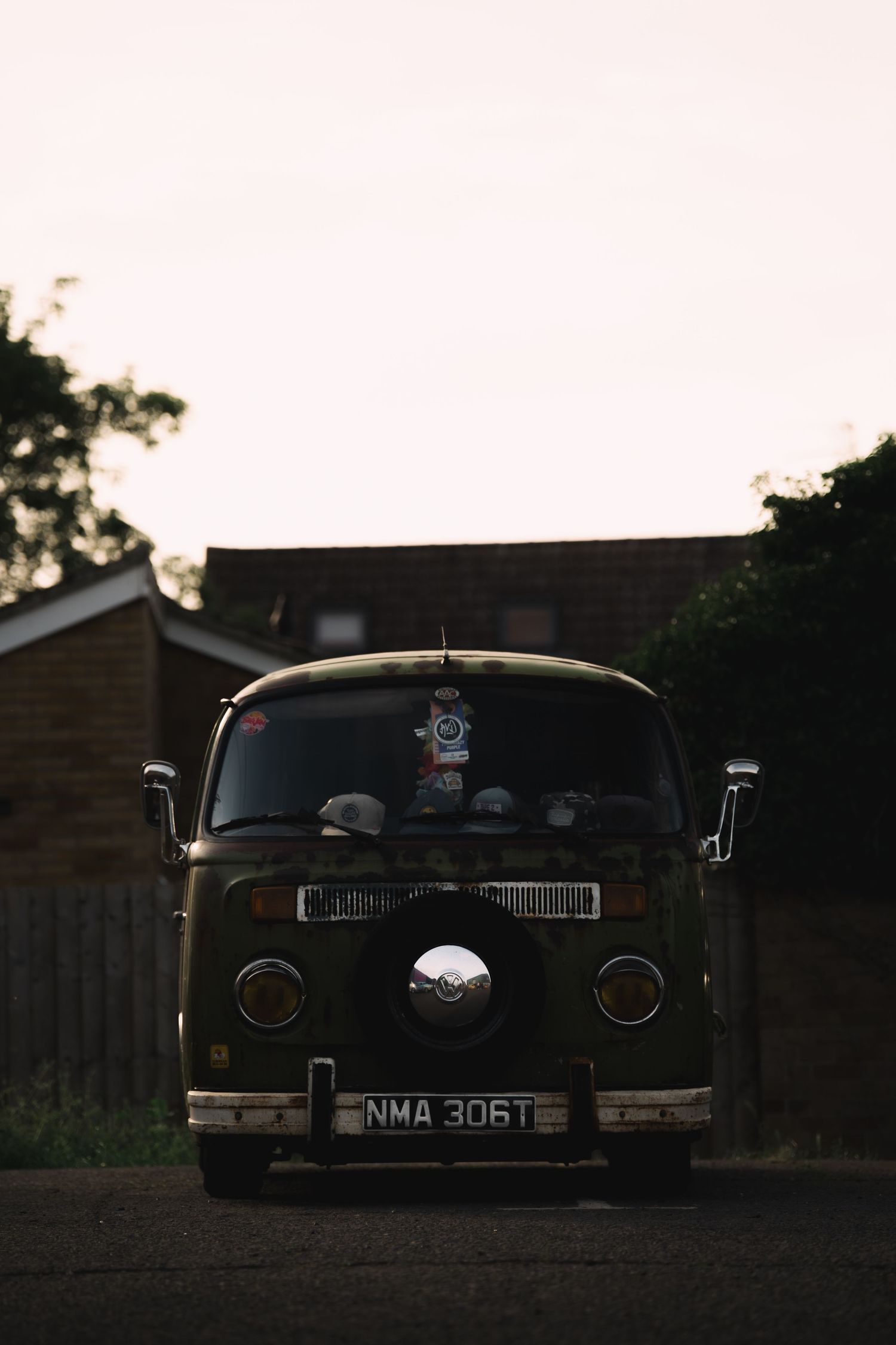Vintage dark green VW camper van with license plate NMA 306T parked on a driveway at dusk.