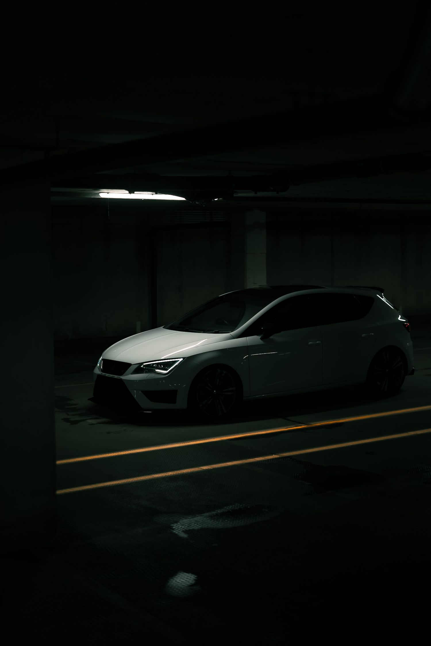 White SEAT Leon Cupra hatchback parked in a dimly lit underground parking garage with orange markings.