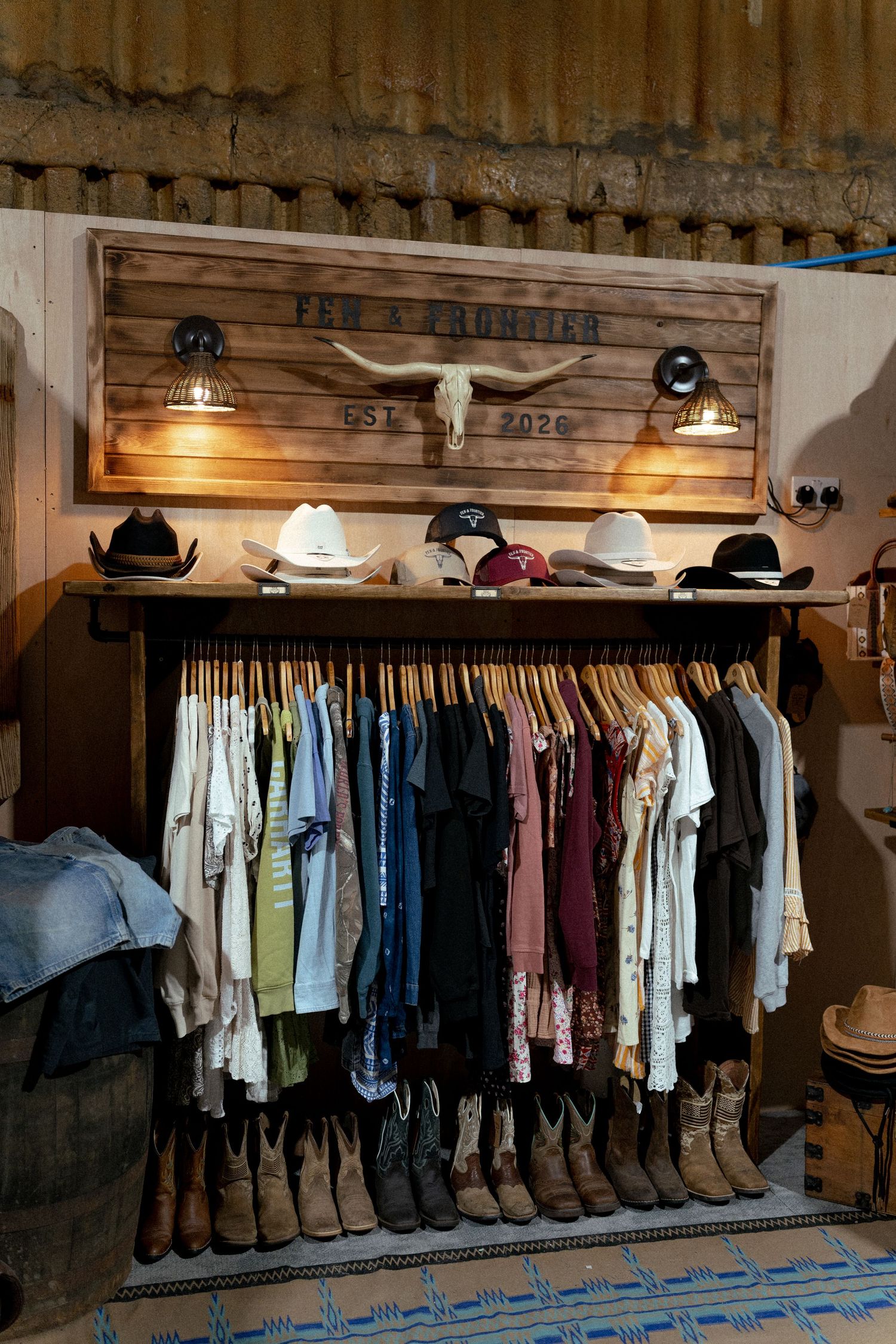 Western boutique display with cowboy hats, boots, and clothing rack beneath a rustic wood sign reading Pen & Frontier Est. 2020.