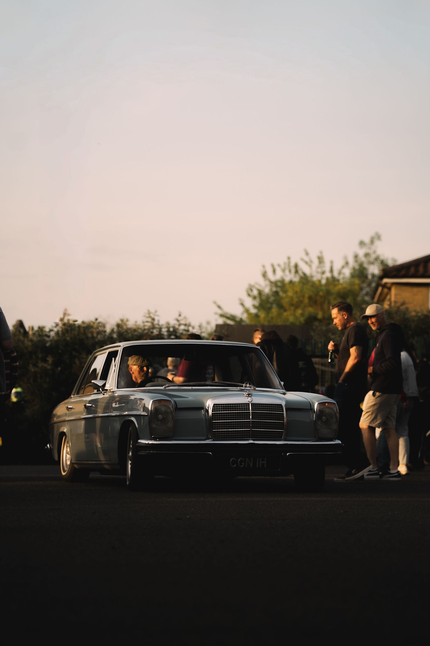 Vintage Mercedes-Benz sedan parked at dusk with people gathered around it during a classic car meet.
