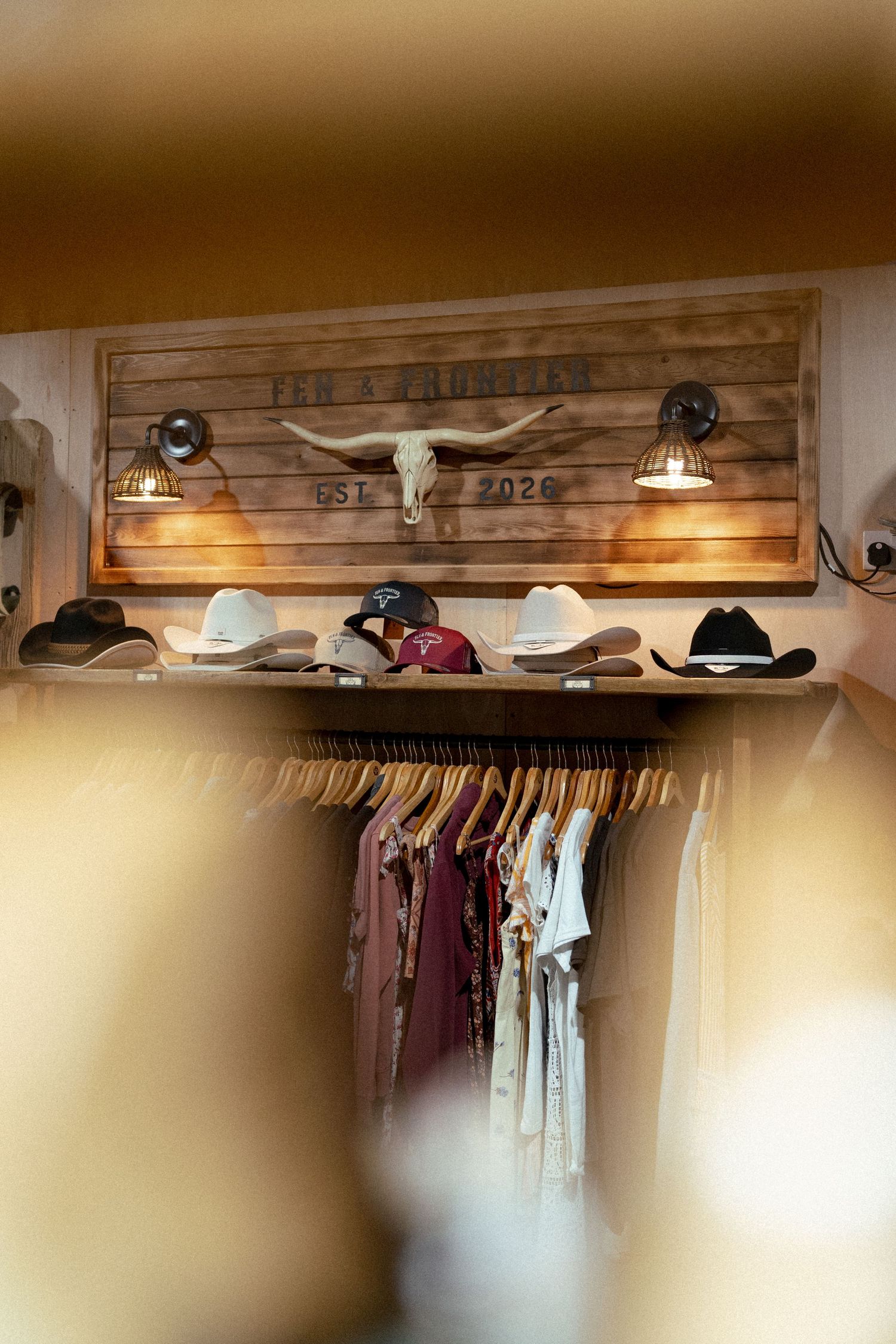 Western boutique interior with cowboy hats, hanging clothes, and a rustic longhorn skull sign reading Est. 2020.