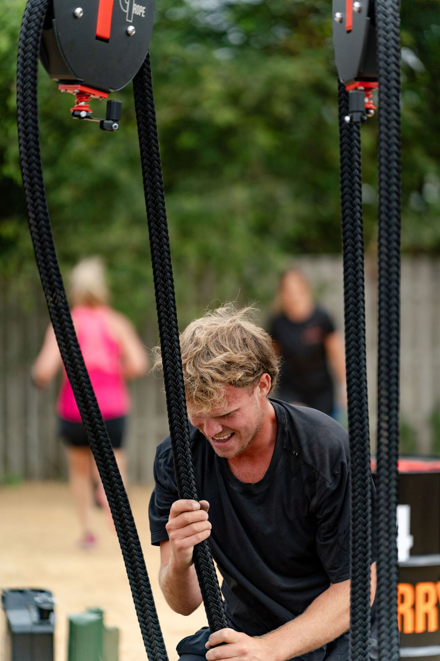 Man straining while pulling heavy ropes at an outdoor fitness obstacle course challenge event.