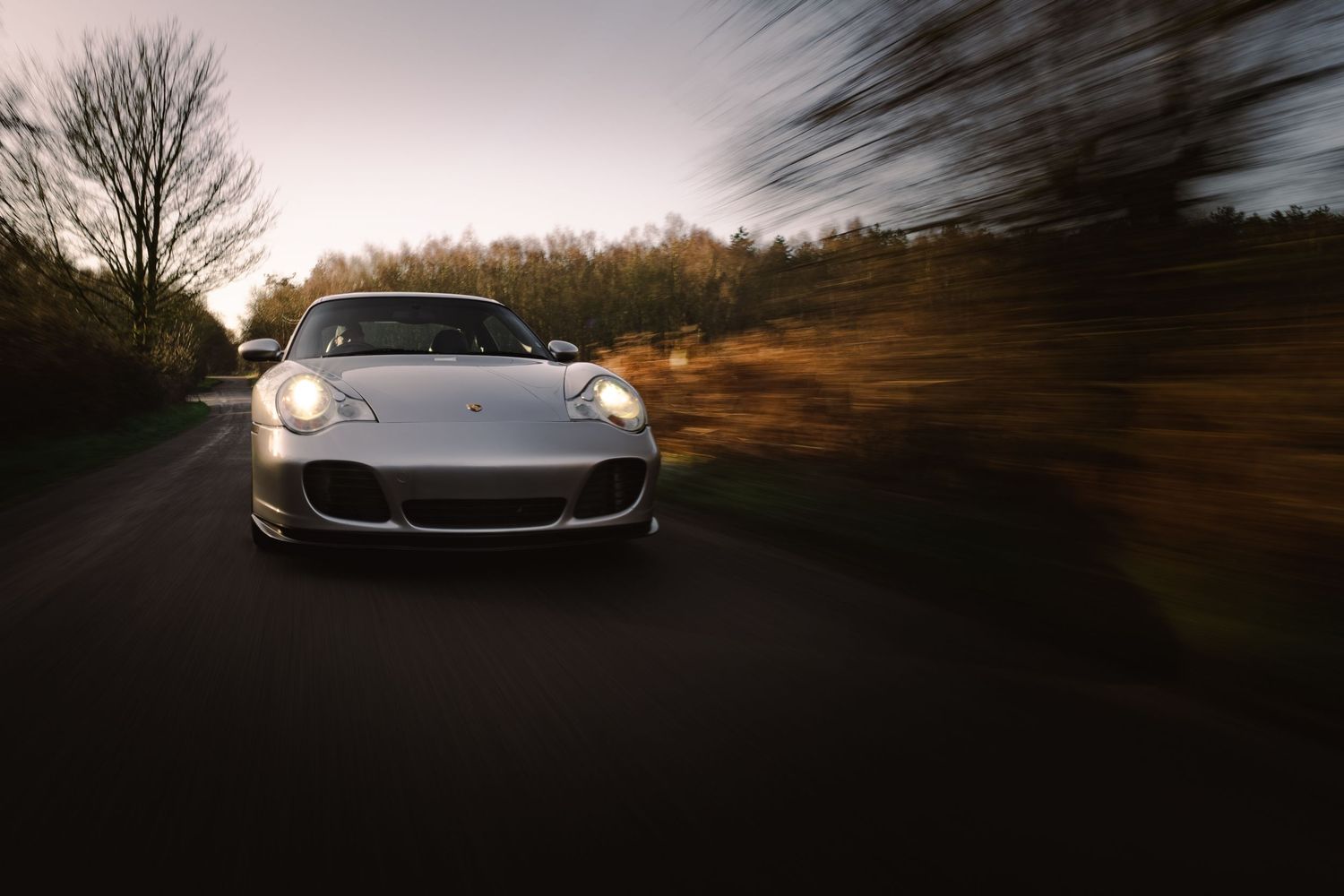 Silver Porsche 911 driving at speed on a country road at sunset with motion blur background.