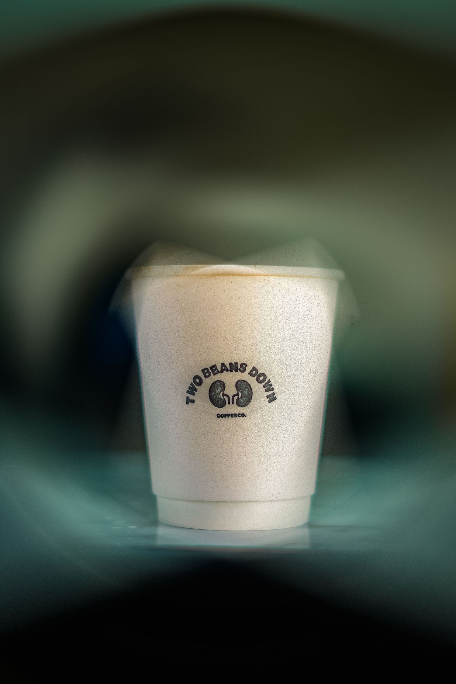 A white Two Beans Down Espresso Co. takeaway coffee cup with creamy latte art on a dark background.
