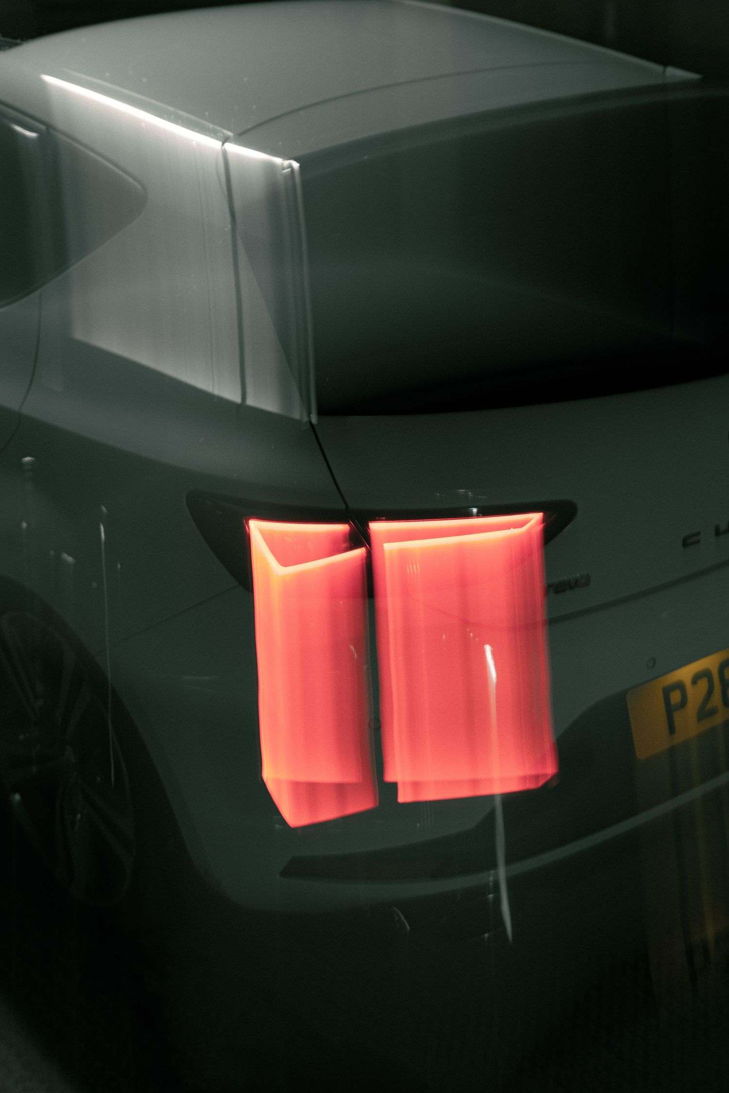 Close-up of bright red rectangular tail lights on a dark grey car in a dimly lit setting.