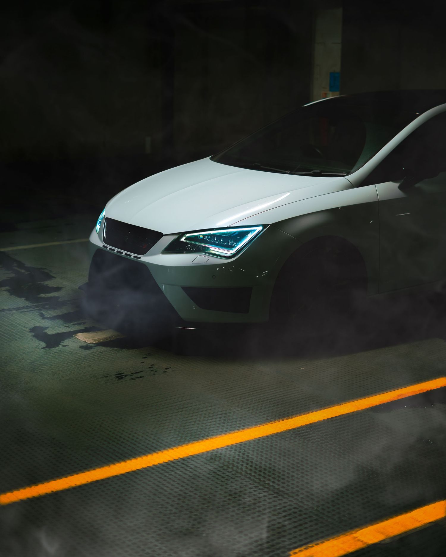 White SEAT Leon Cupra with LED headlights emitting smoke in a dimly lit underground parking garage.