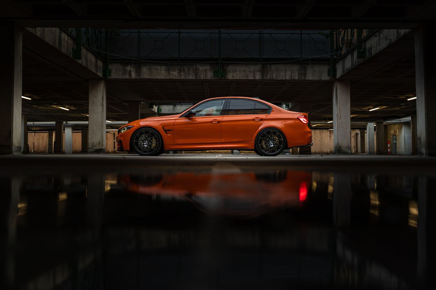 Orange BMW M4 coupe parked in a dark garage with a vivid reflection on the wet floor.