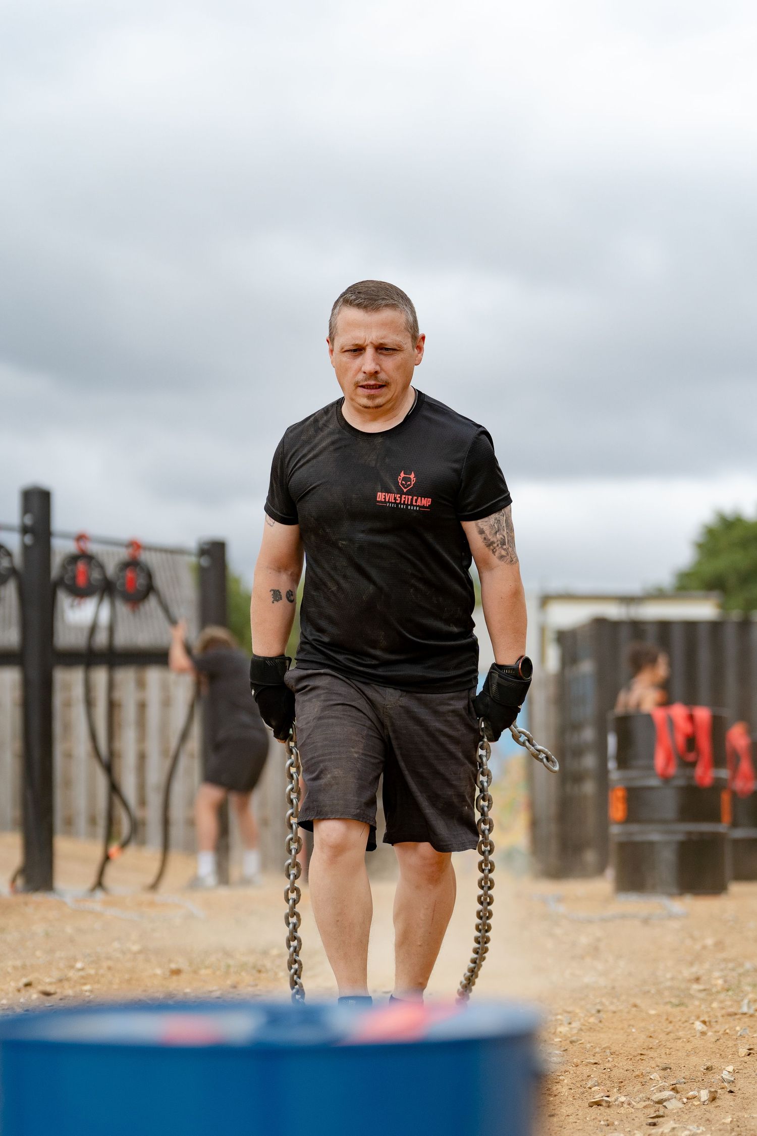 Man in black t-shirt pulling heavy chains during outdoor fitness training at a boot camp obstacle course.
