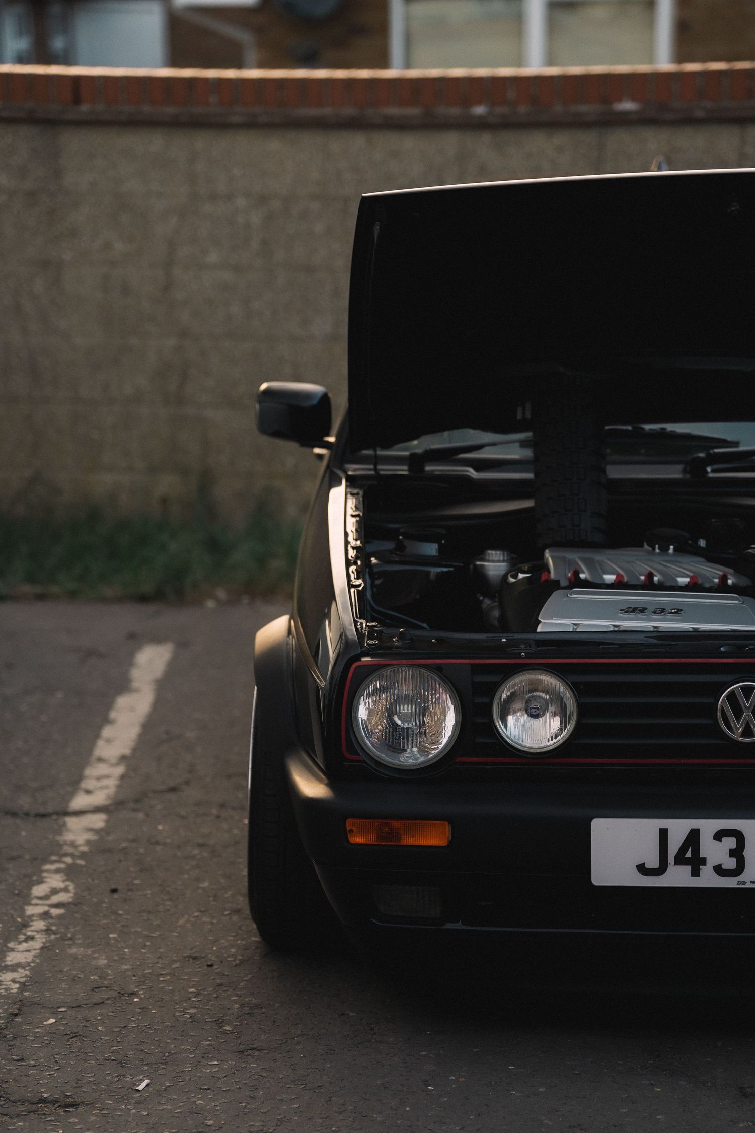 Black Volkswagen Golf MK2 with hood open showing engine bay, parked on street with J43 license plate.