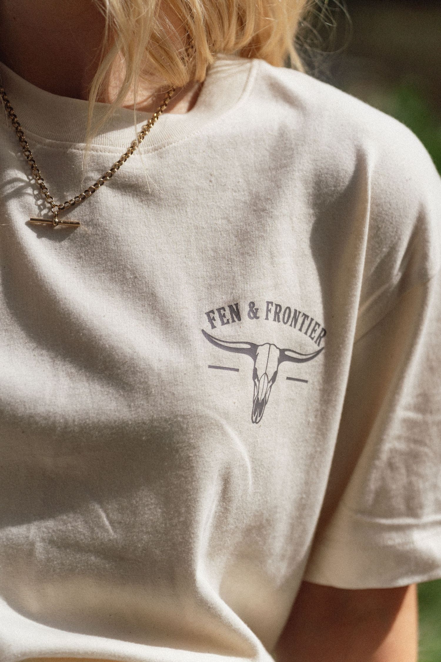 Cream vintage-style Fen & Frontier t-shirt featuring a longhorn skull graphic, worn with a gold chain necklace.