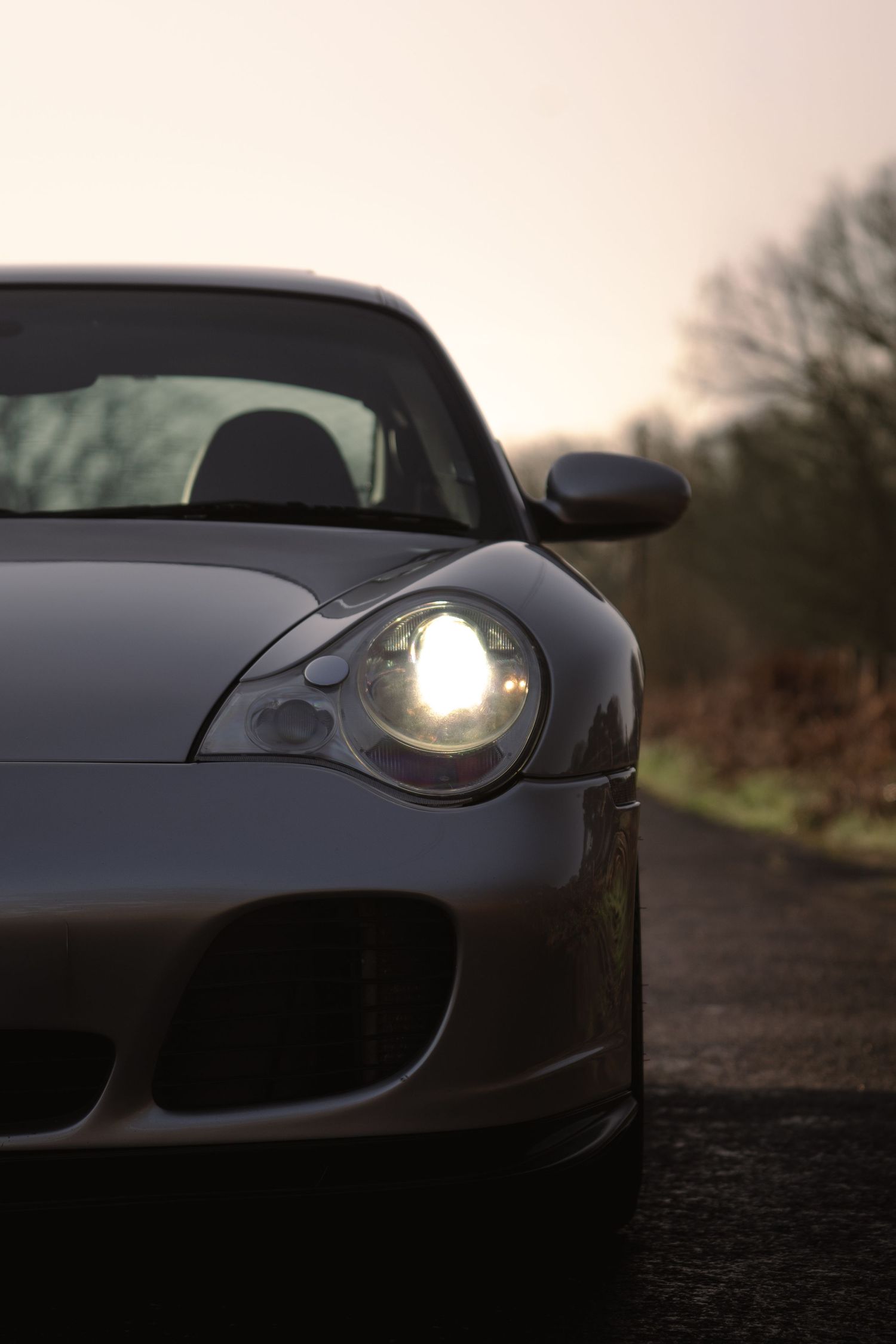 Close-up of Porsche 911 Turbo headlight on a country road at sunset.