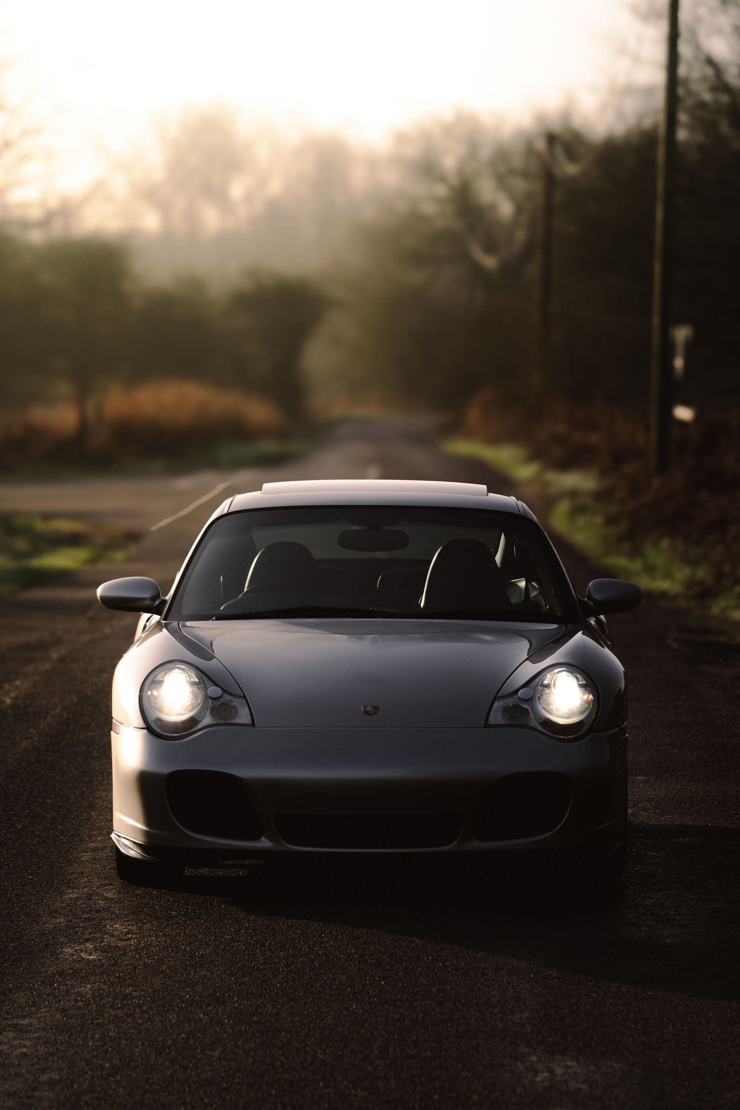 Front view of silver Porsche 911 Turbo with headlights on a misty road.