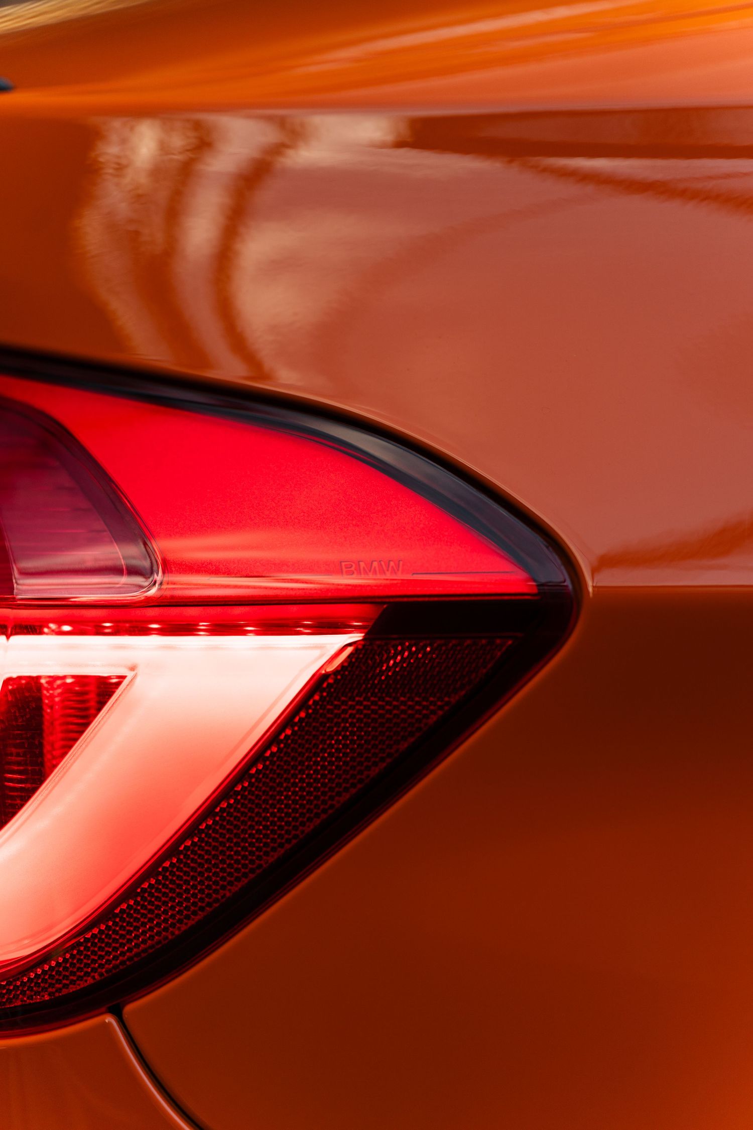 Close-up of a sleek red tail light on a glossy orange car, showcasing modern automotive design.