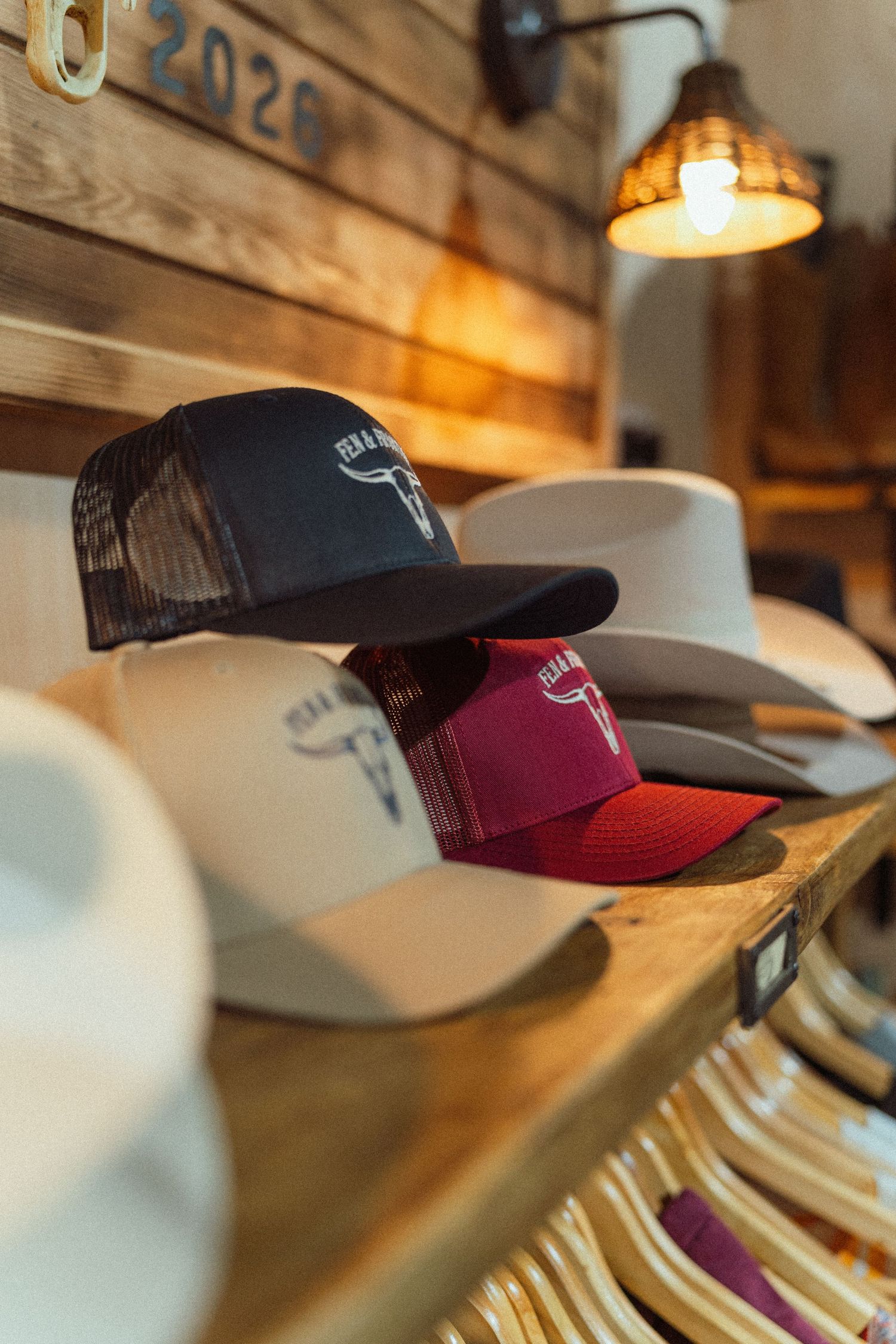 Western hats and trucker caps displayed on wooden shelves in a rustic store with warm lighting.
