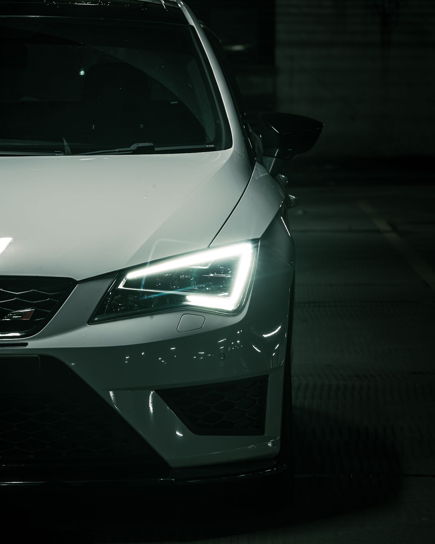 Close-up of a white SEAT Leon Cupra front headlight with sharp LED daytime running lights in darkness.