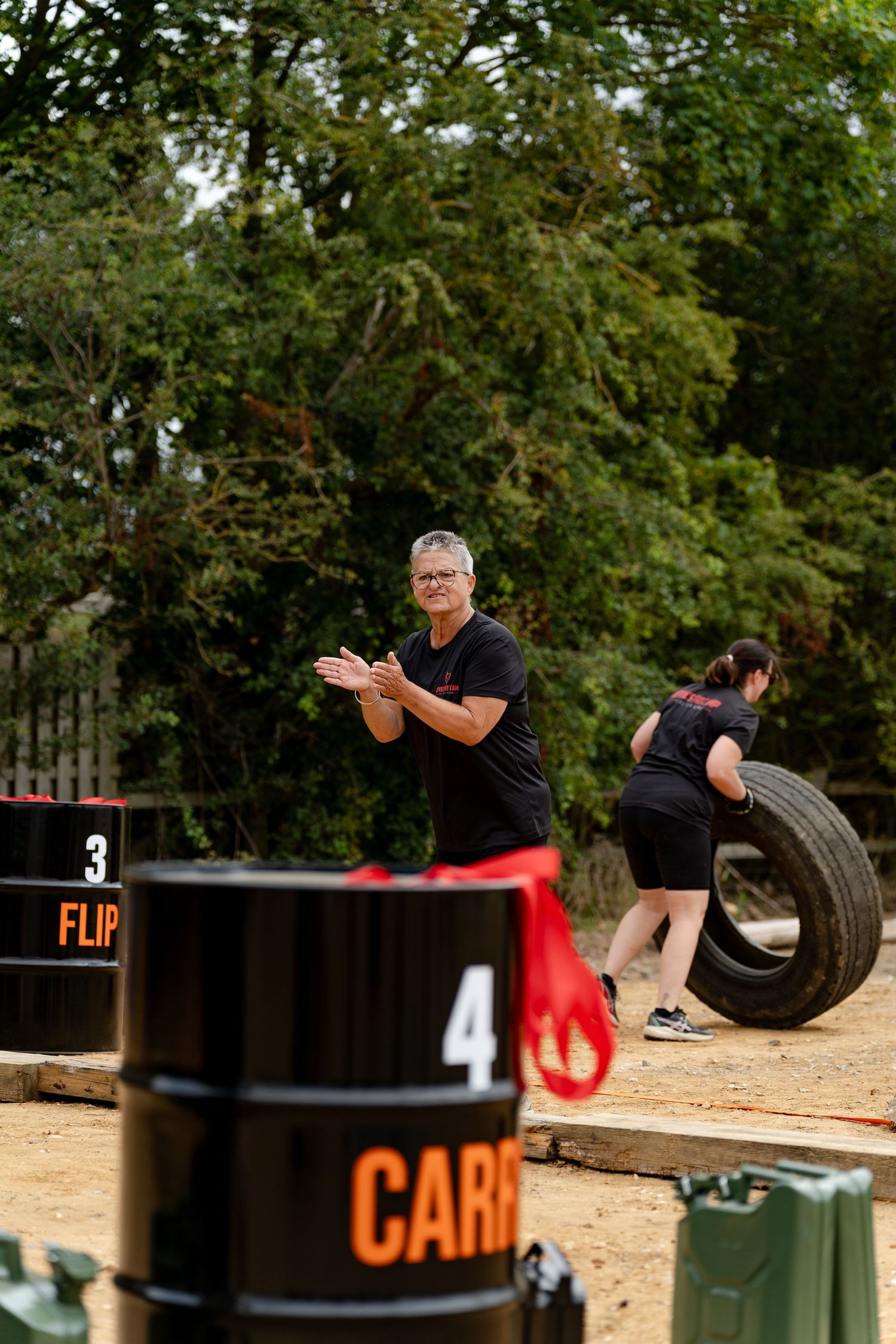 Outdoor fitness challenge with participants flipping tires and carrying barrels at a obstacle course event.