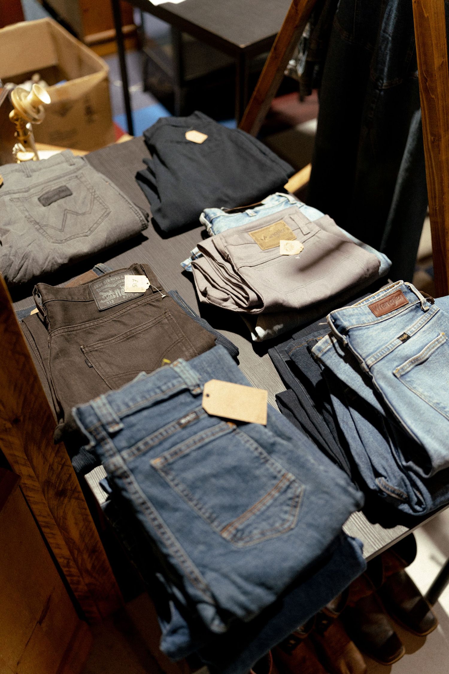 Folded denim jeans with price tags displayed on a wooden shelf in a retail clothing store.