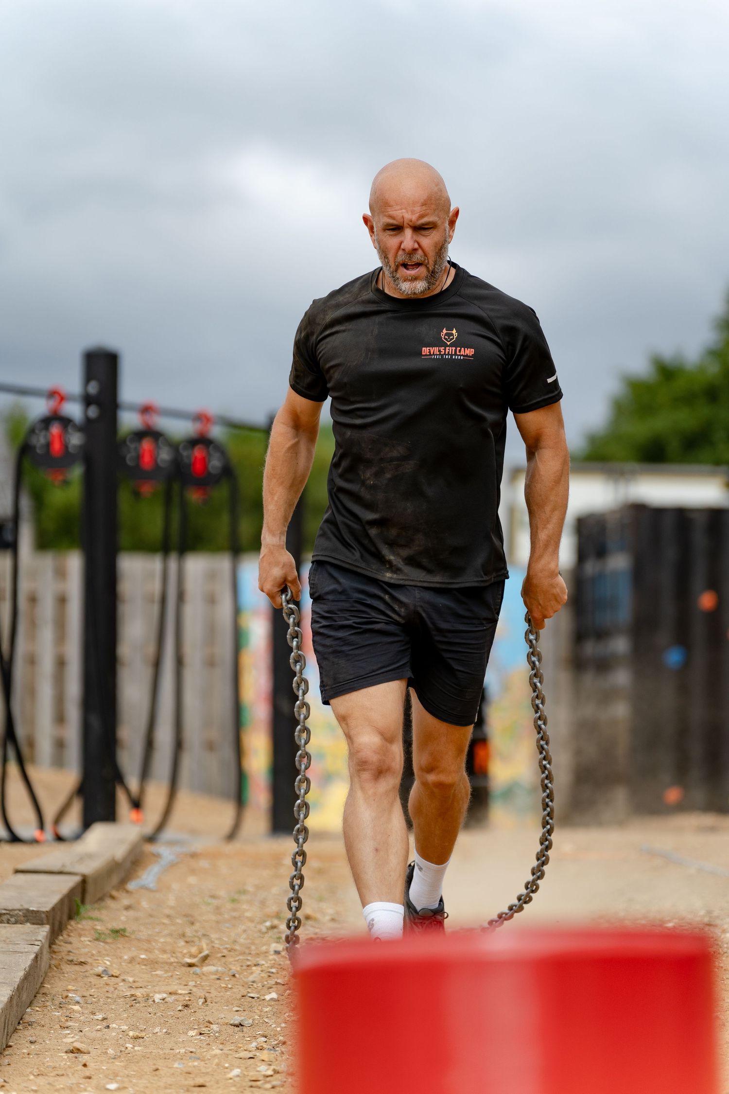 Determined bald man pulling heavy chains during an outdoor fitness obstacle course workout event.