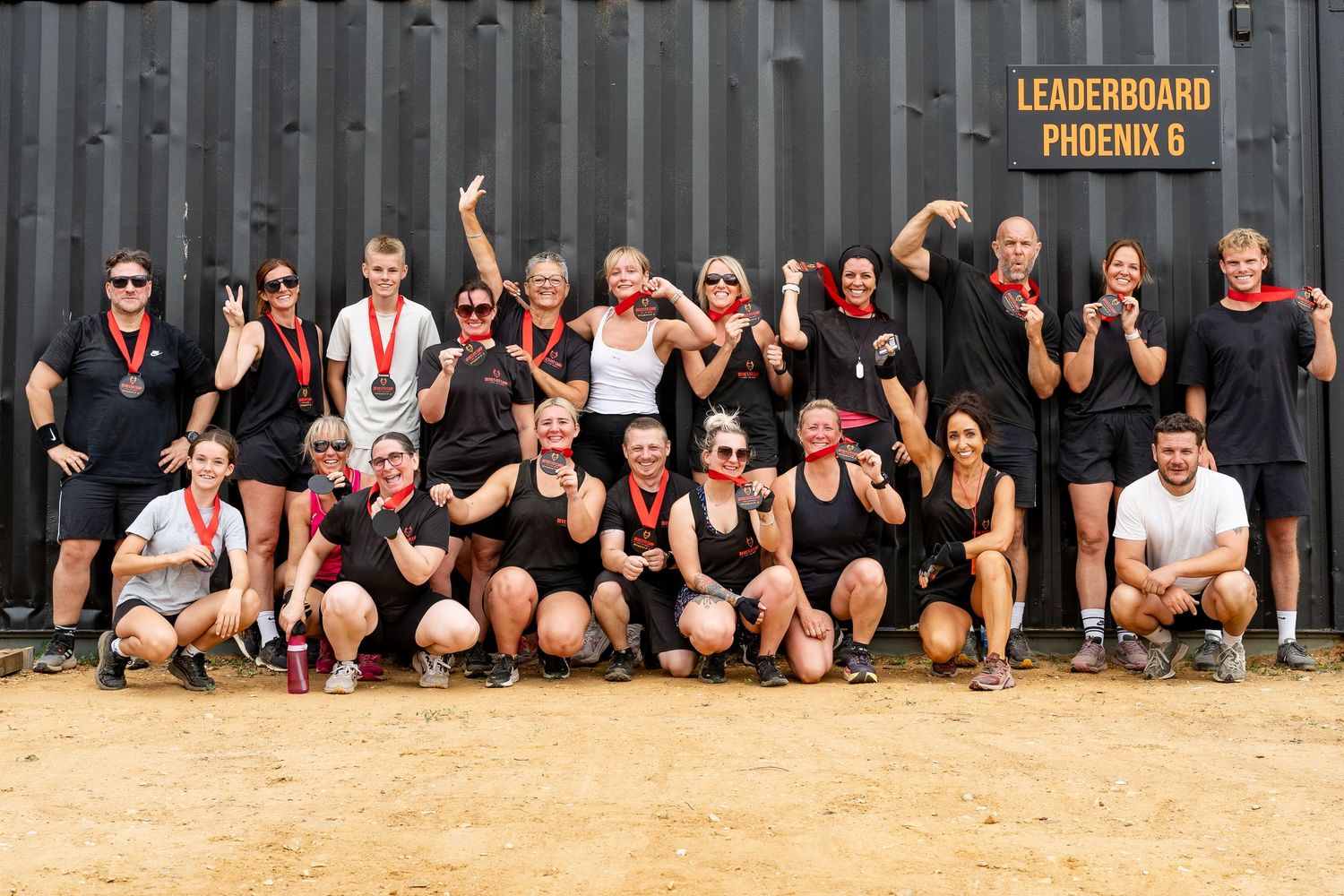 Group of athletes posing with medals in front of a Leaderboard Phoenix 6 sign after completing a fitness challenge.